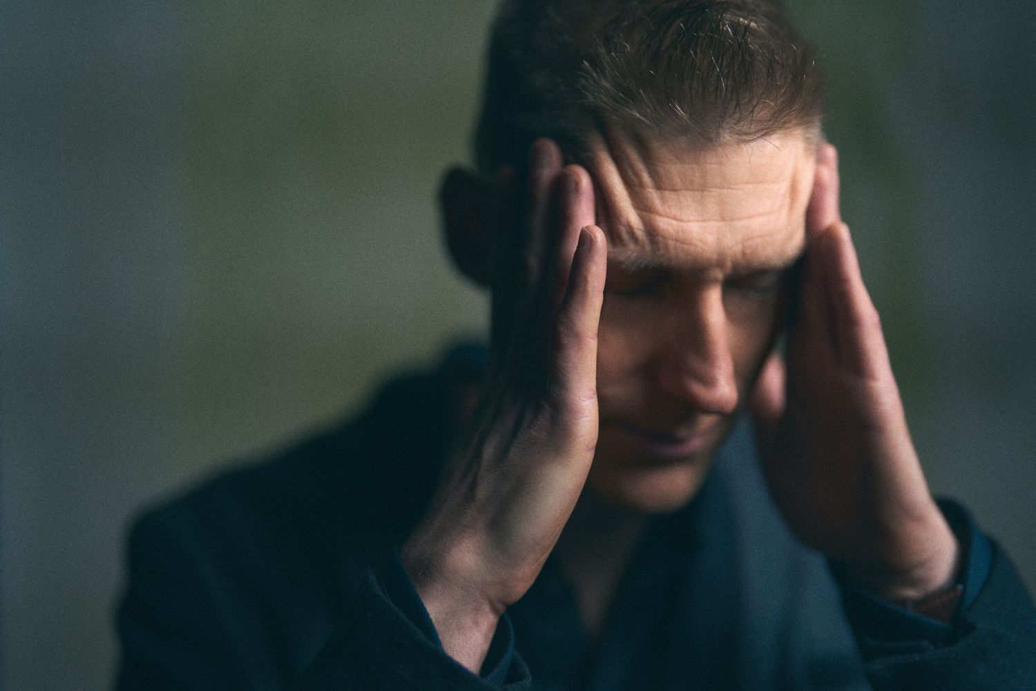 Stressed man holding his head in his hands, showing signs of anxiety, headache, or mental health struggles.