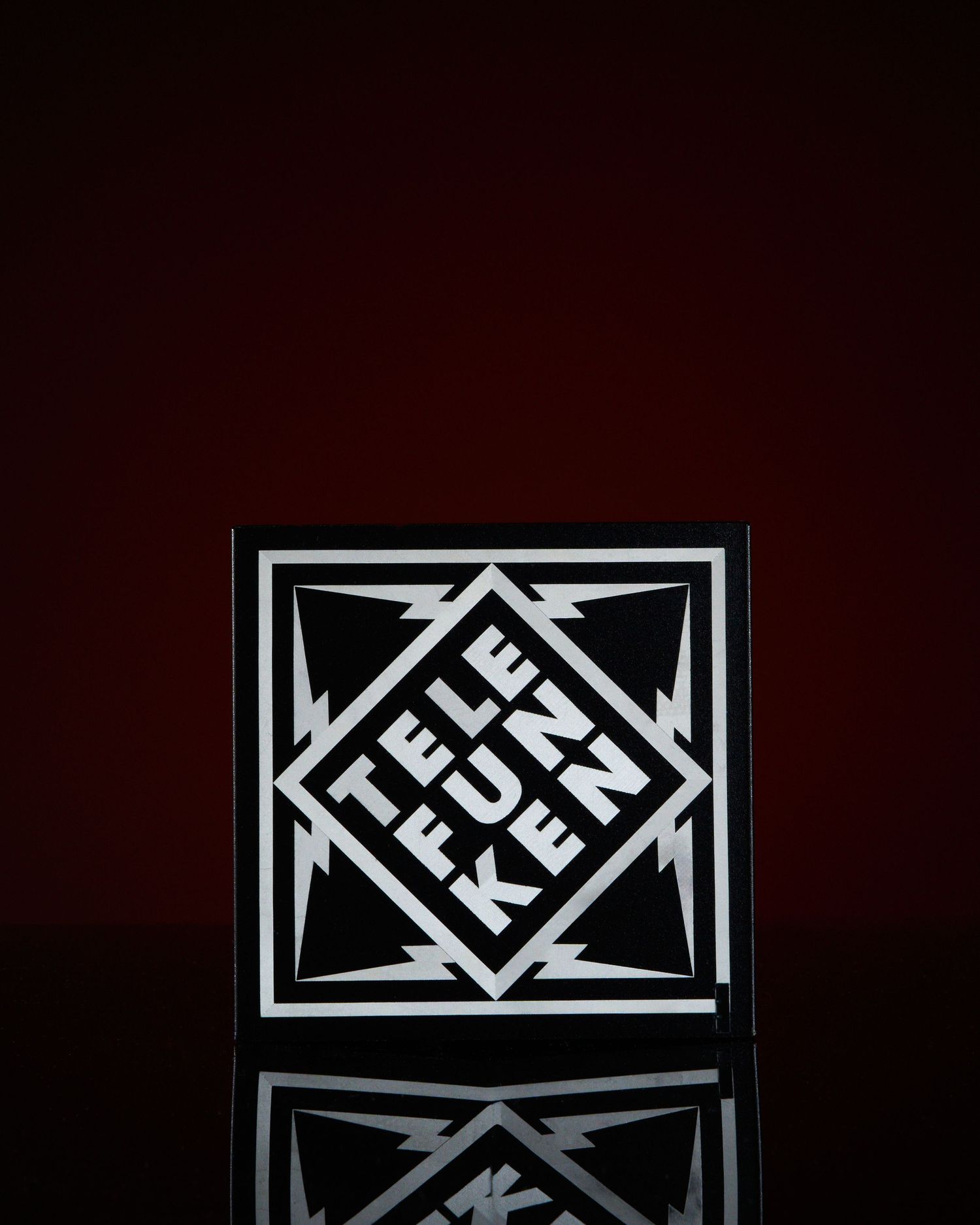 Telefunken brand logo box with bold black and white diamond design and lightning bolts on dark red background.