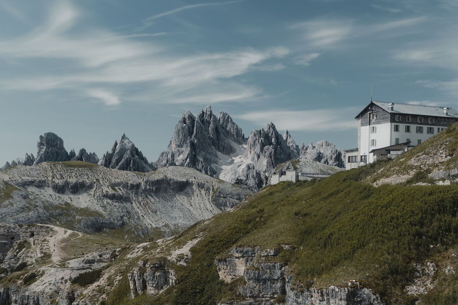 Alpine mountain refuge building nestled below jagged Dolomite peaks on a rocky hillside.