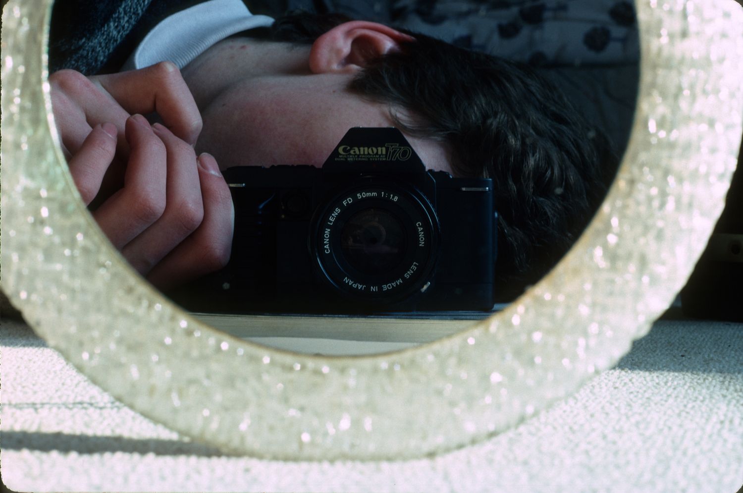 A person takes a Canon camera self-portrait reflected in a round decorative mirror with pearl border.