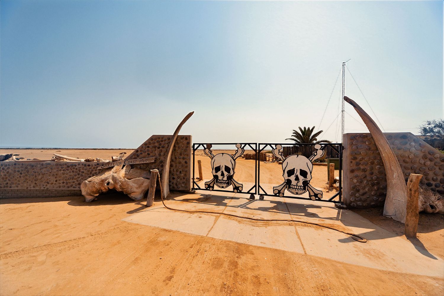Decorative gate featuring skull and crossbones with elephant tusks on a sandy desert terrace.