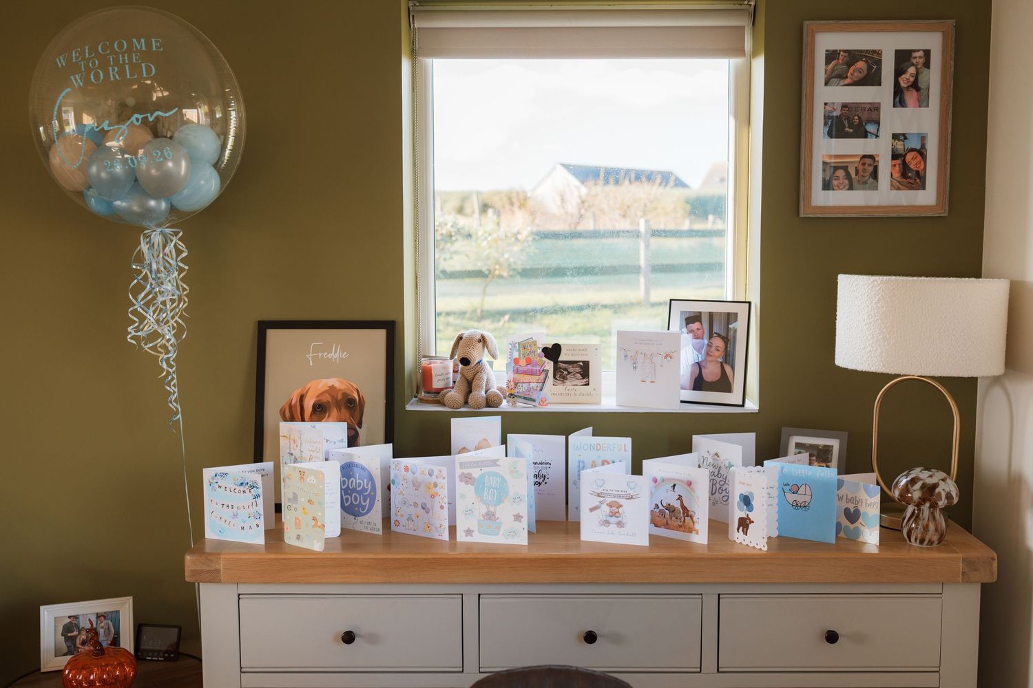 Birthday cards and framed photos displayed on a white chest of drawers beside a window, with a balloon bouquet in the corner.