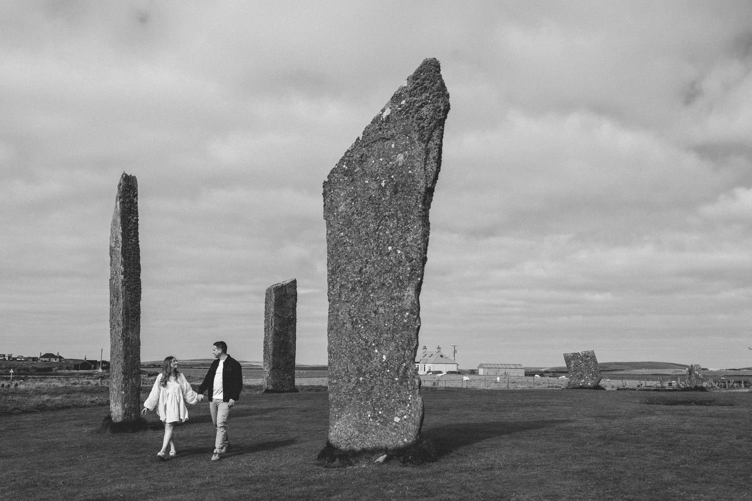 A black and white photo of a couple walking past towering ancient standing stones on open moorland.