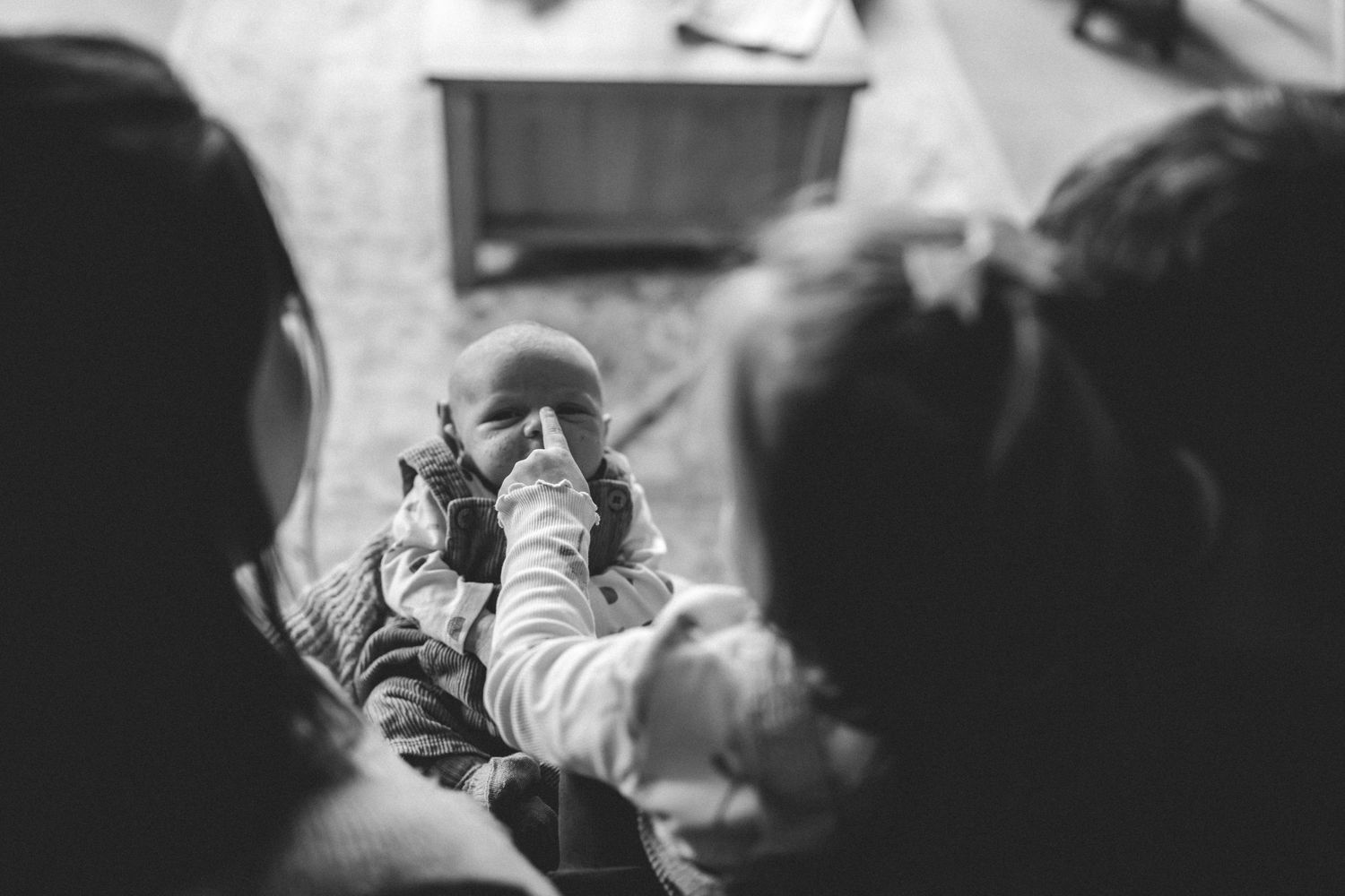 Black and white photo of a baby in a knit sweater being gently touched on the nose by a child in the foreground.