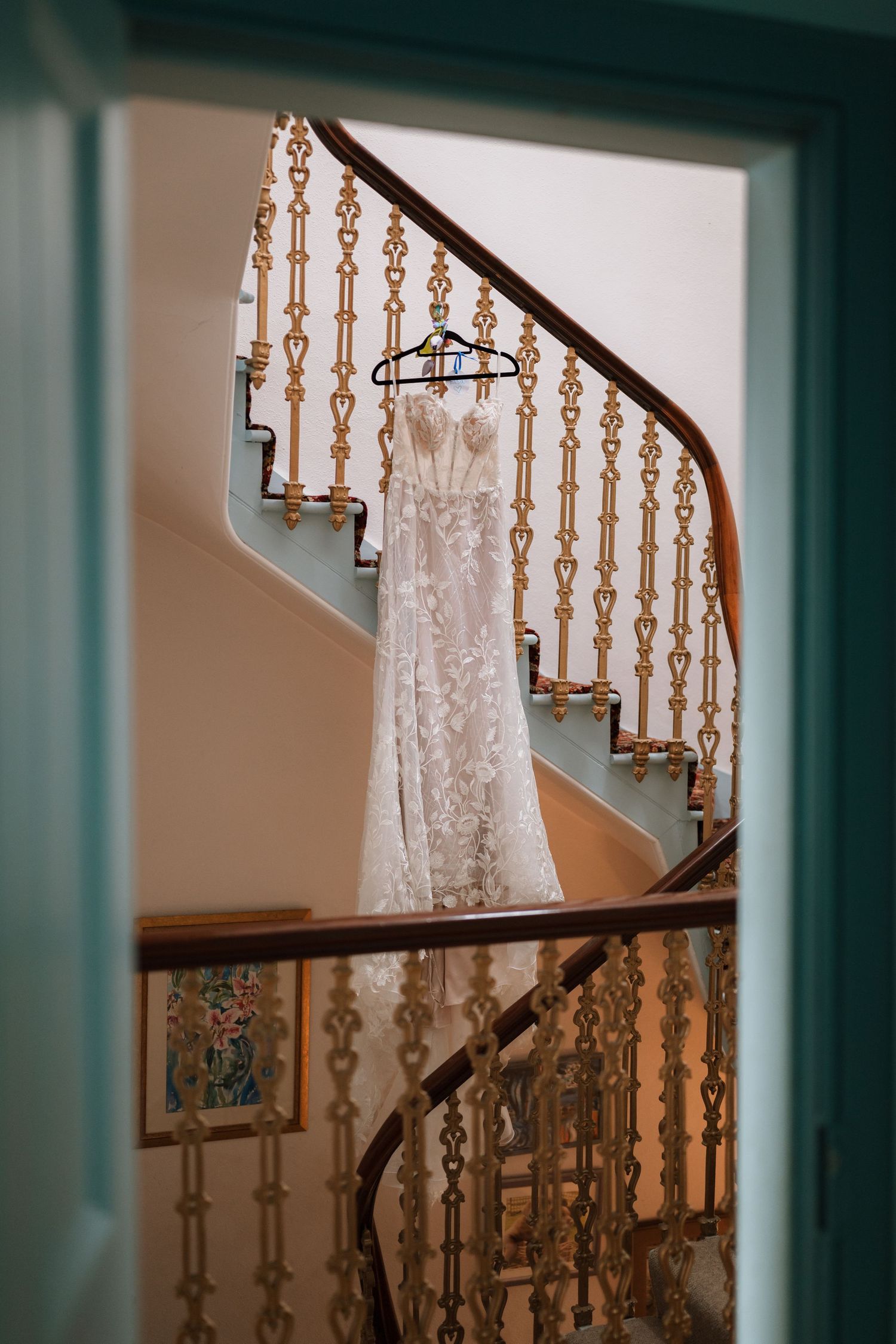 Lace wedding dress hanging on a hanger beside an ornate golden banister and curved staircase.