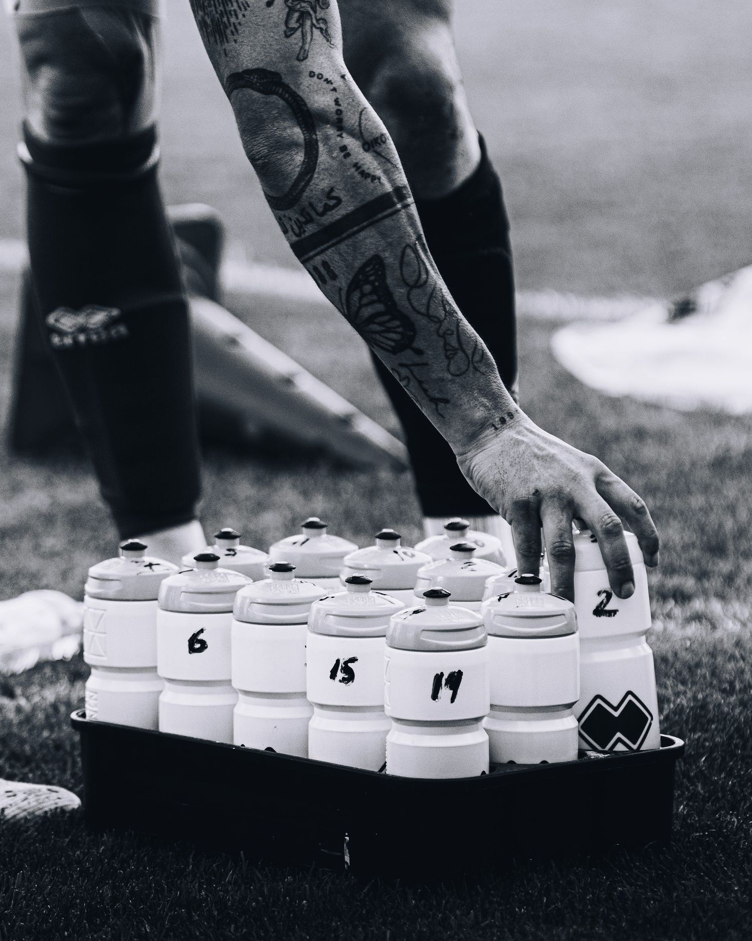 Tattooed athlete reaching for numbered water bottles on a tray during a sports match.