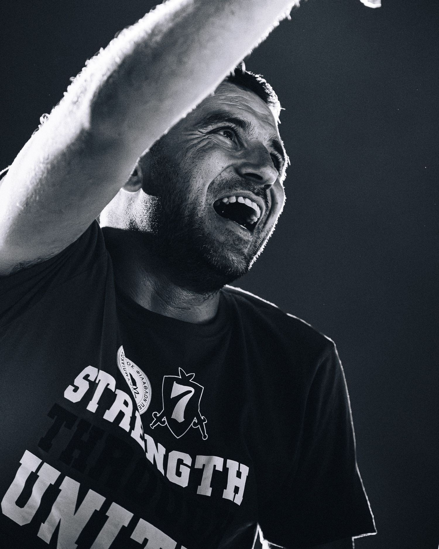 Black and white photo of a man in a Strength Unity shirt cheering with his arm raised.