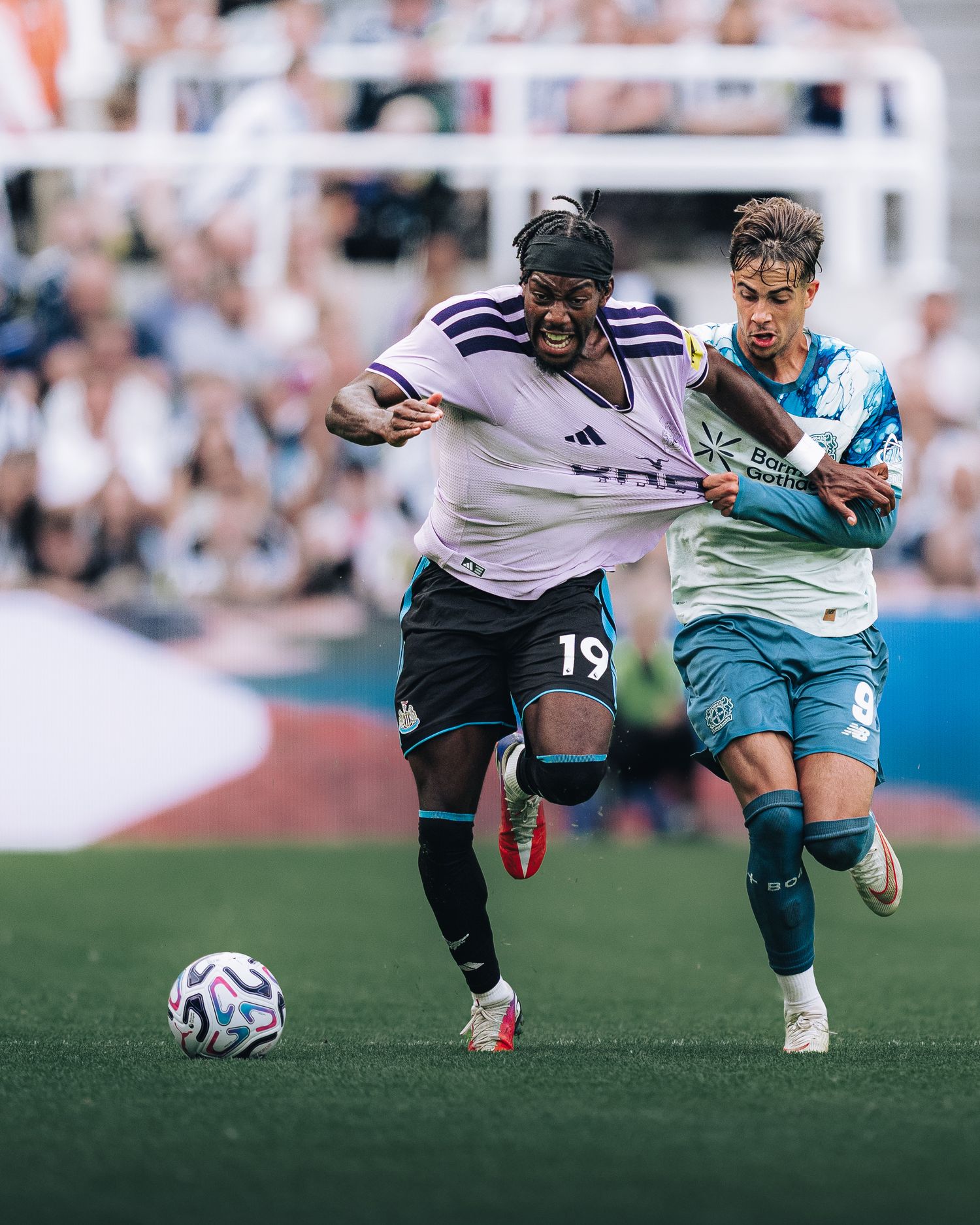 Newcastle United player number 19 battles for ball against Leverkusen opponent during match.