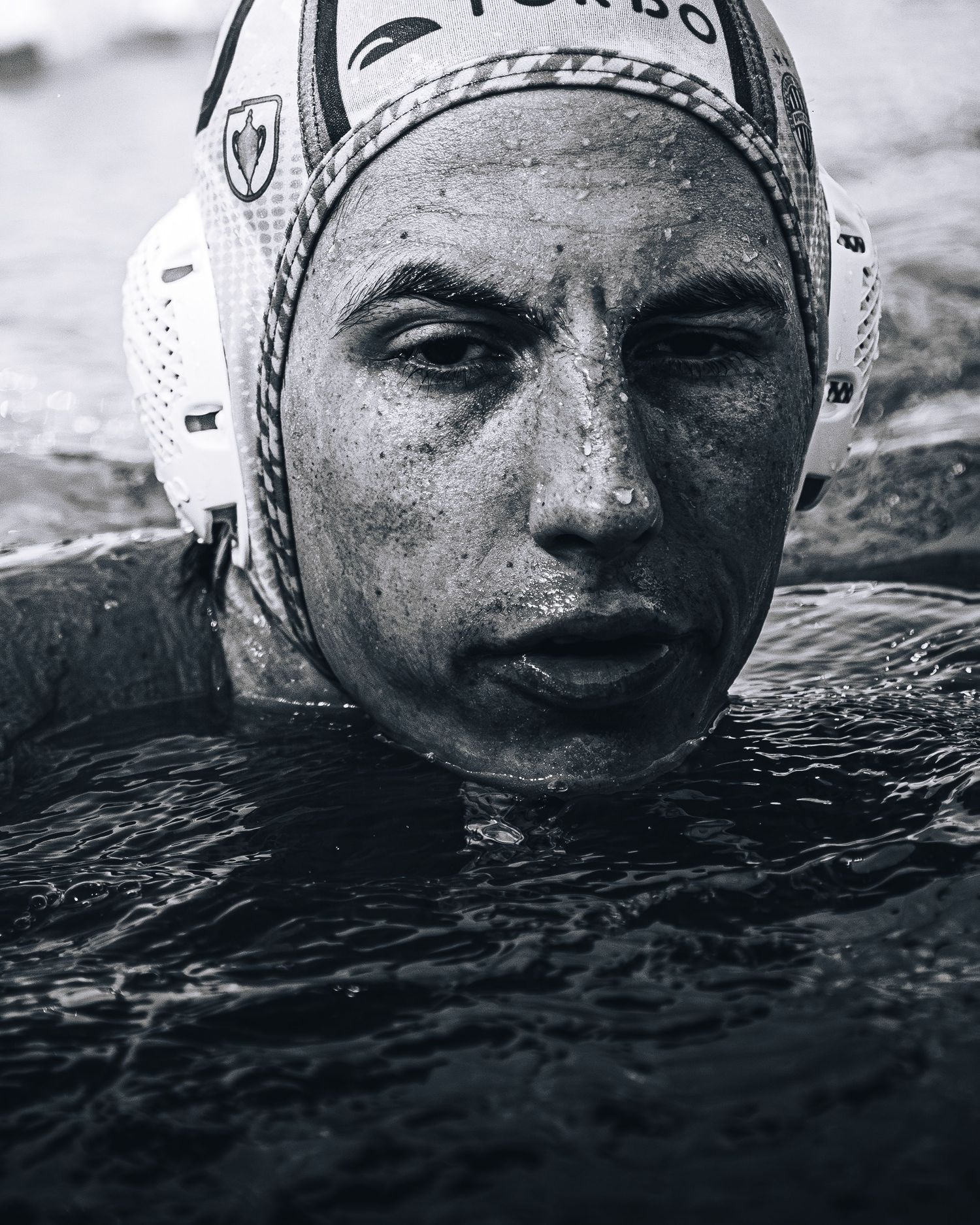 Black and white close-up of a water polo player in a swim cap emerging from the water.