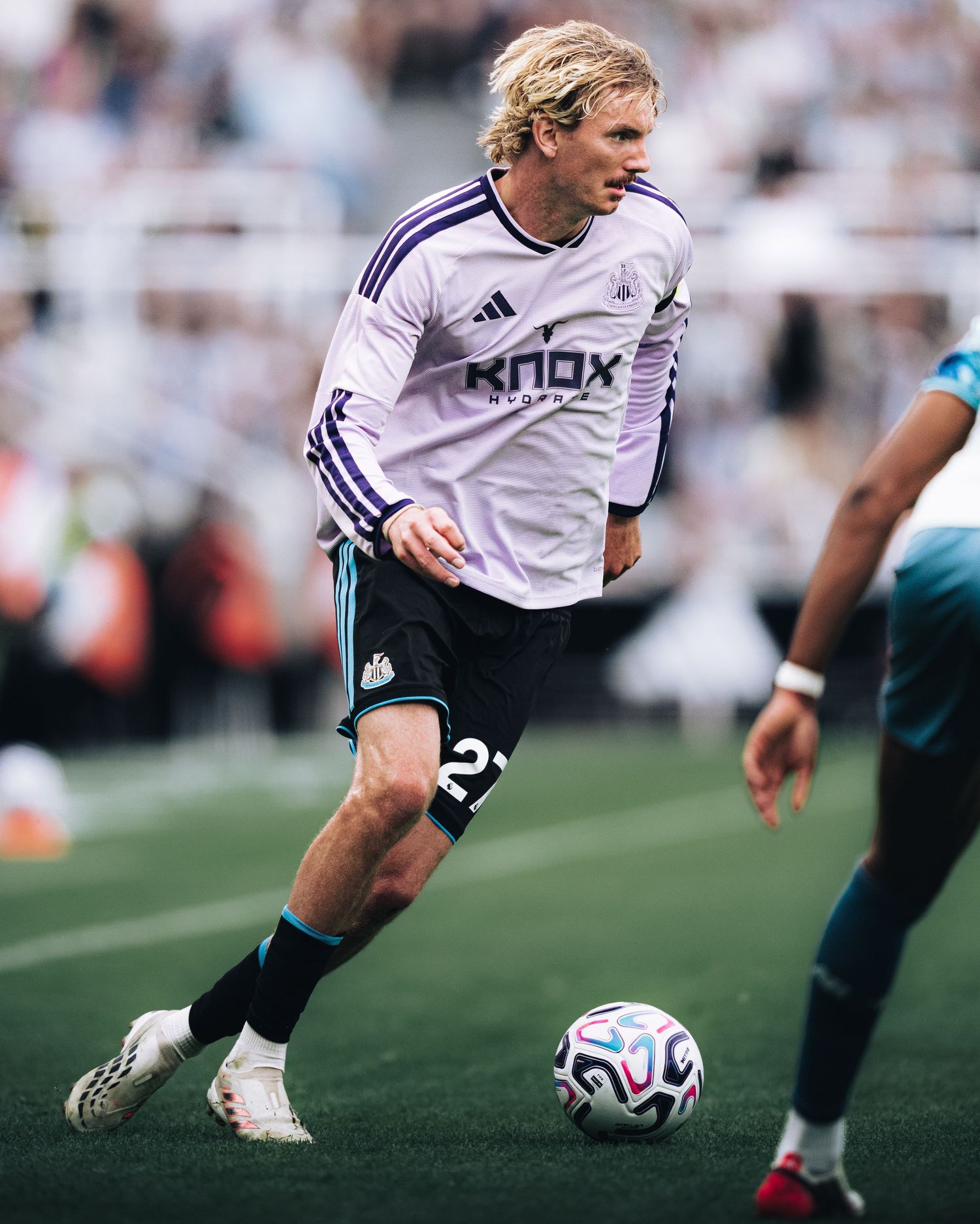 Blonde soccer player in white Knox Adidas jersey number 22 controlling ball during stadium match.
