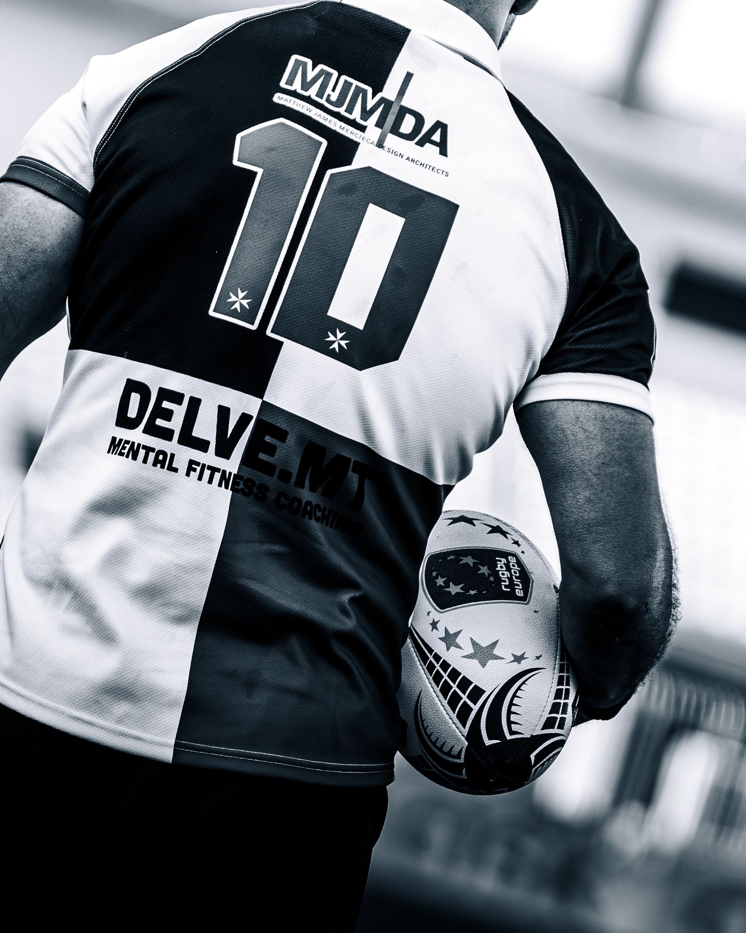 Black and white rear view of rugby player number 10 holding helmet on field.