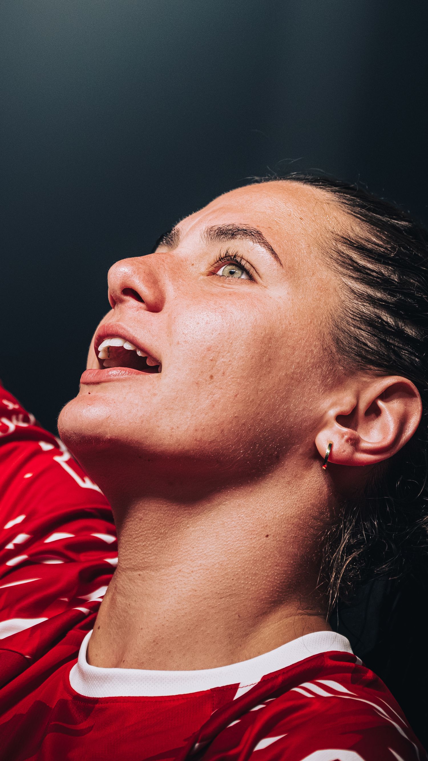 Close-up of a female athlete in a red jersey looking up with an expression of joy.