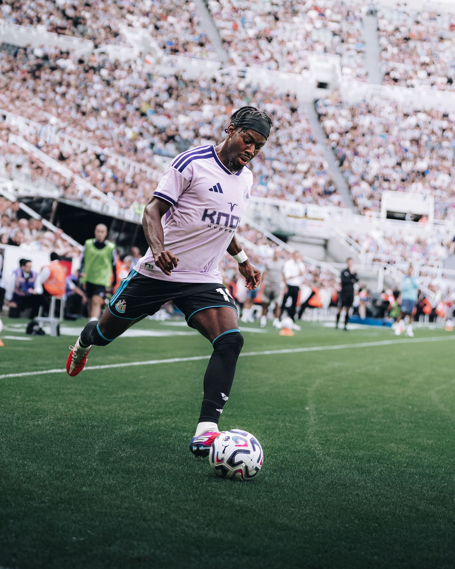 Soccer player in white Knox jersey dribbling ball on green pitch in front of large stadium crowd.