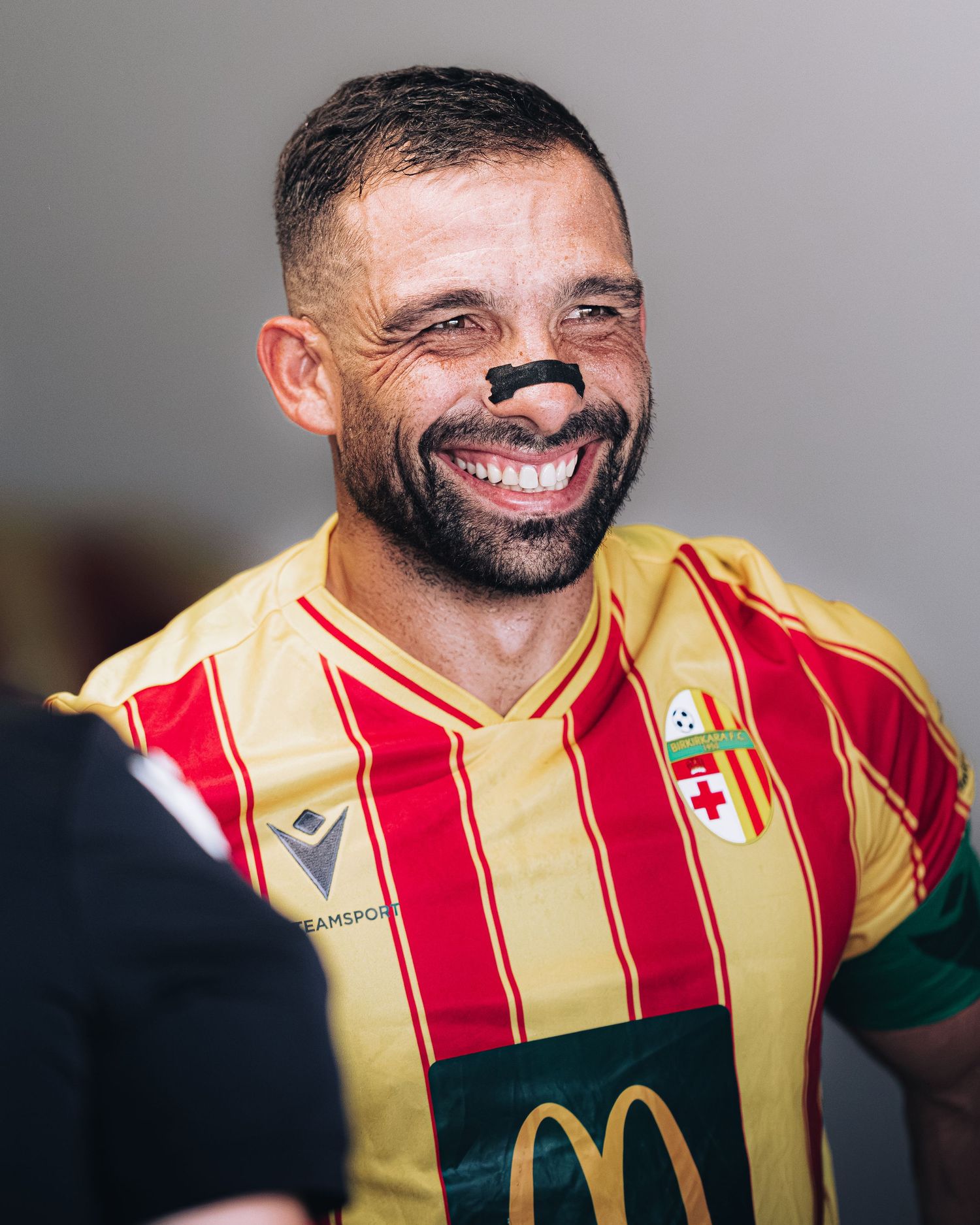 Soccer player in red and yellow striped kit smiles with face paint.