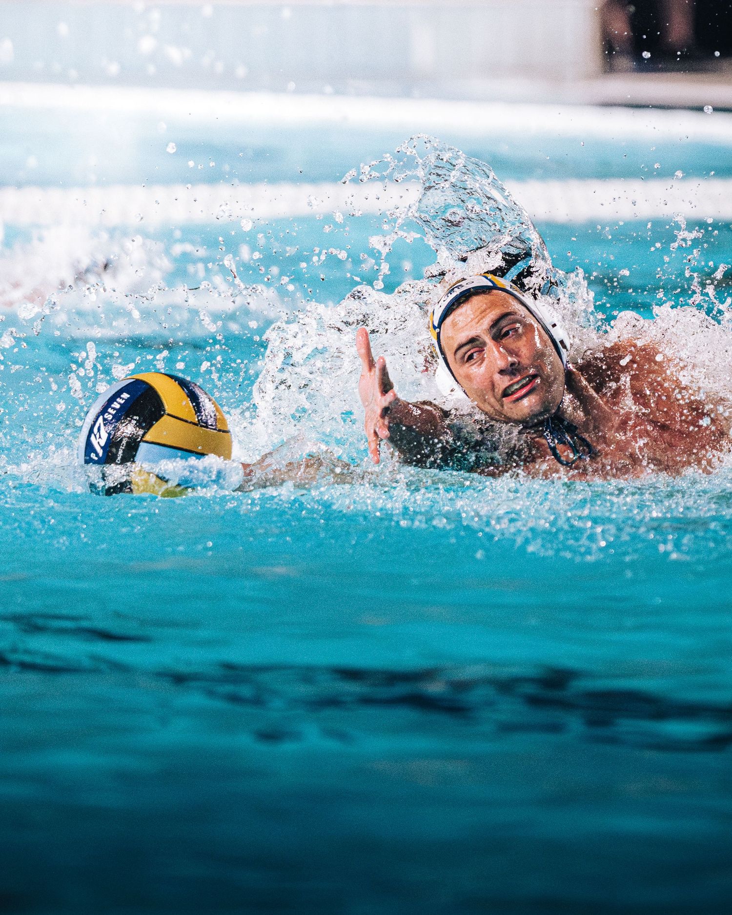 Water polo player swimming aggressively toward the ball during a competitive match.