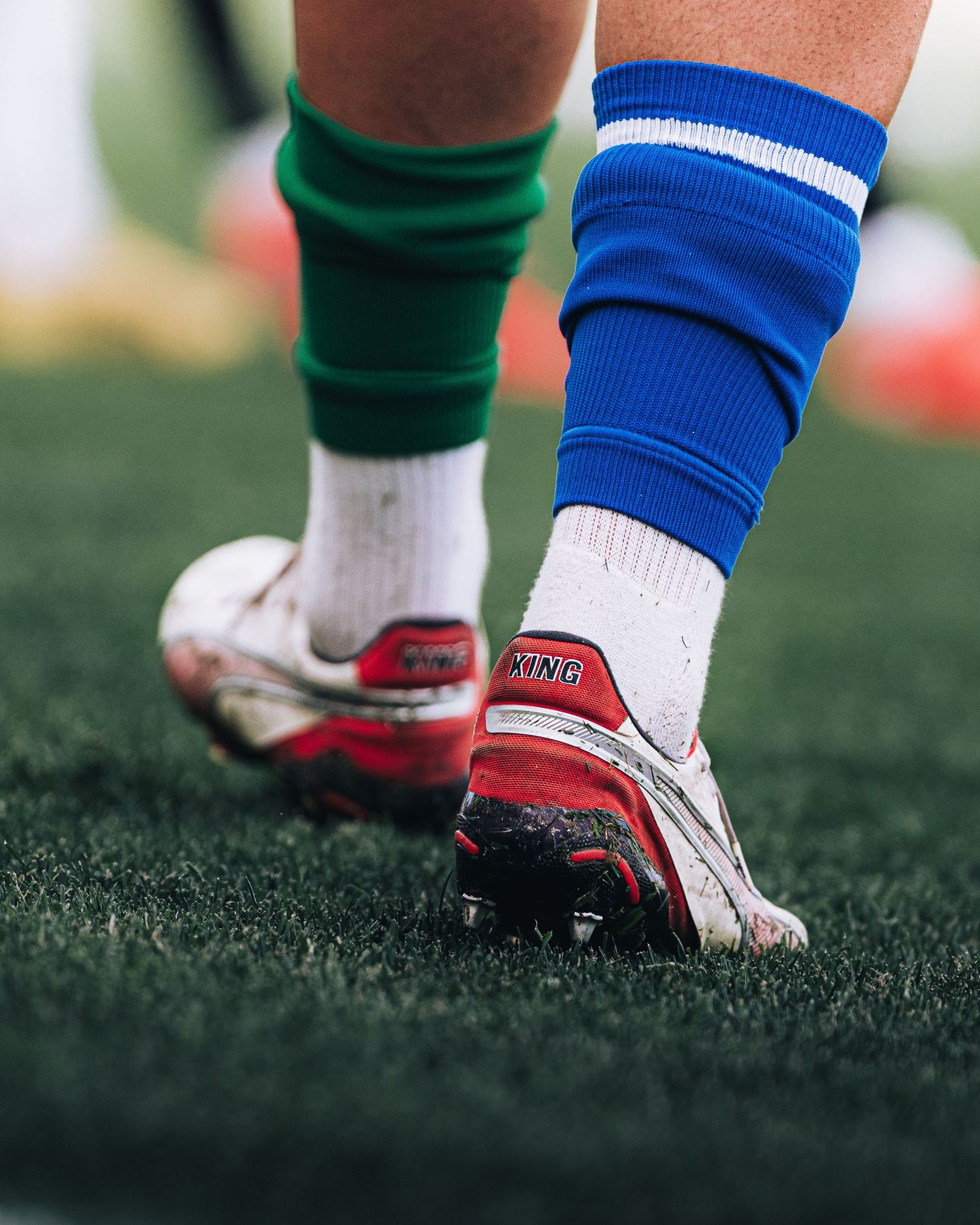 Close-up of football cleats with blue socks on green artificial turf during a match.