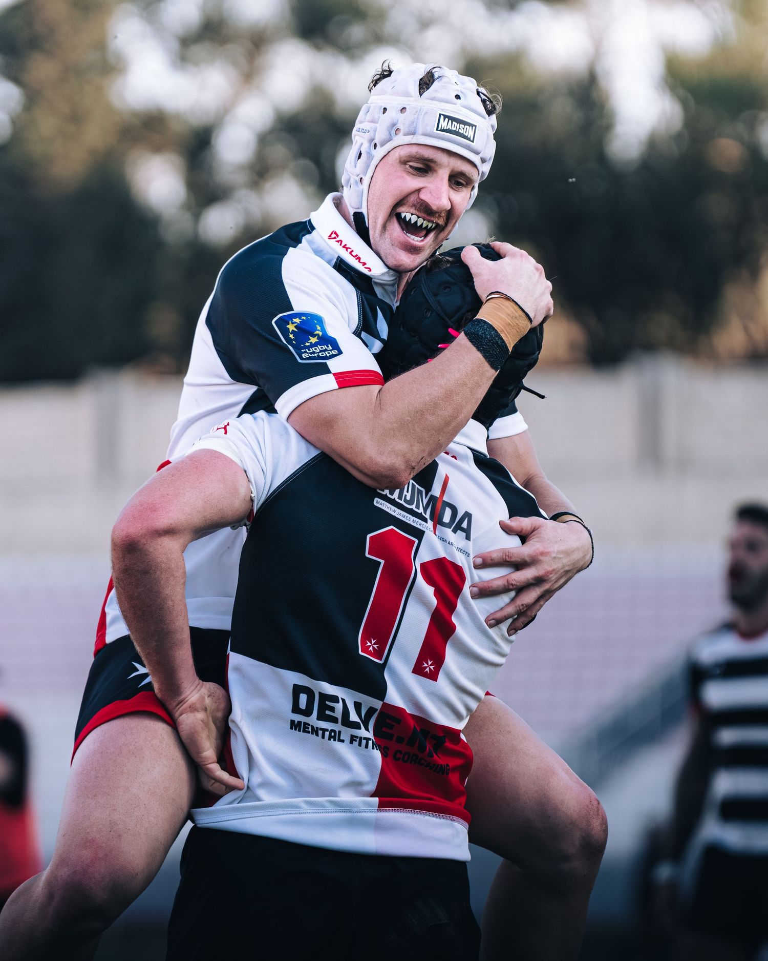Two rugby players in black and white jerseys celebrate joyfully after a successful match.