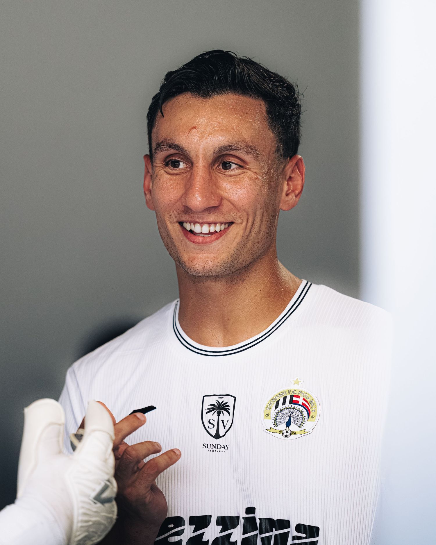 Smiling soccer player in white kit poses for portrait photo.