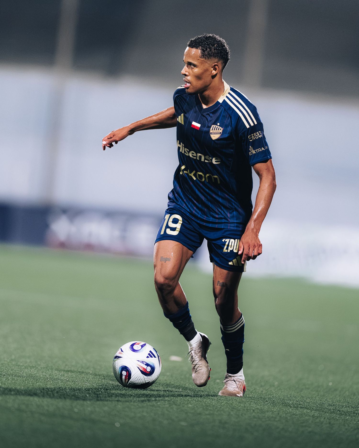 Young footballer wearing navy blue number 19 jersey dribbling ball on green artificial turf.