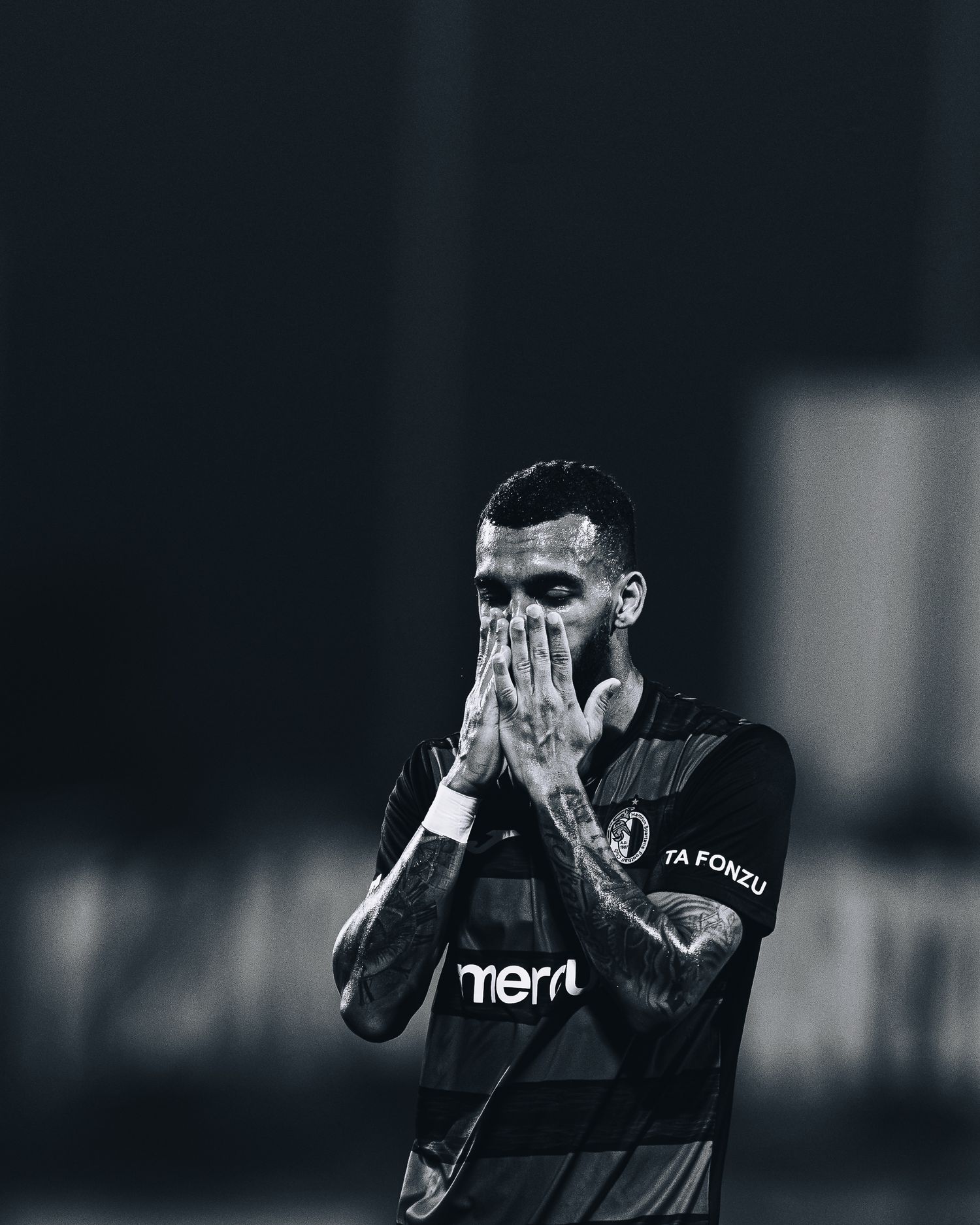 Black and white photo of emotional soccer player covering face with hands during game.