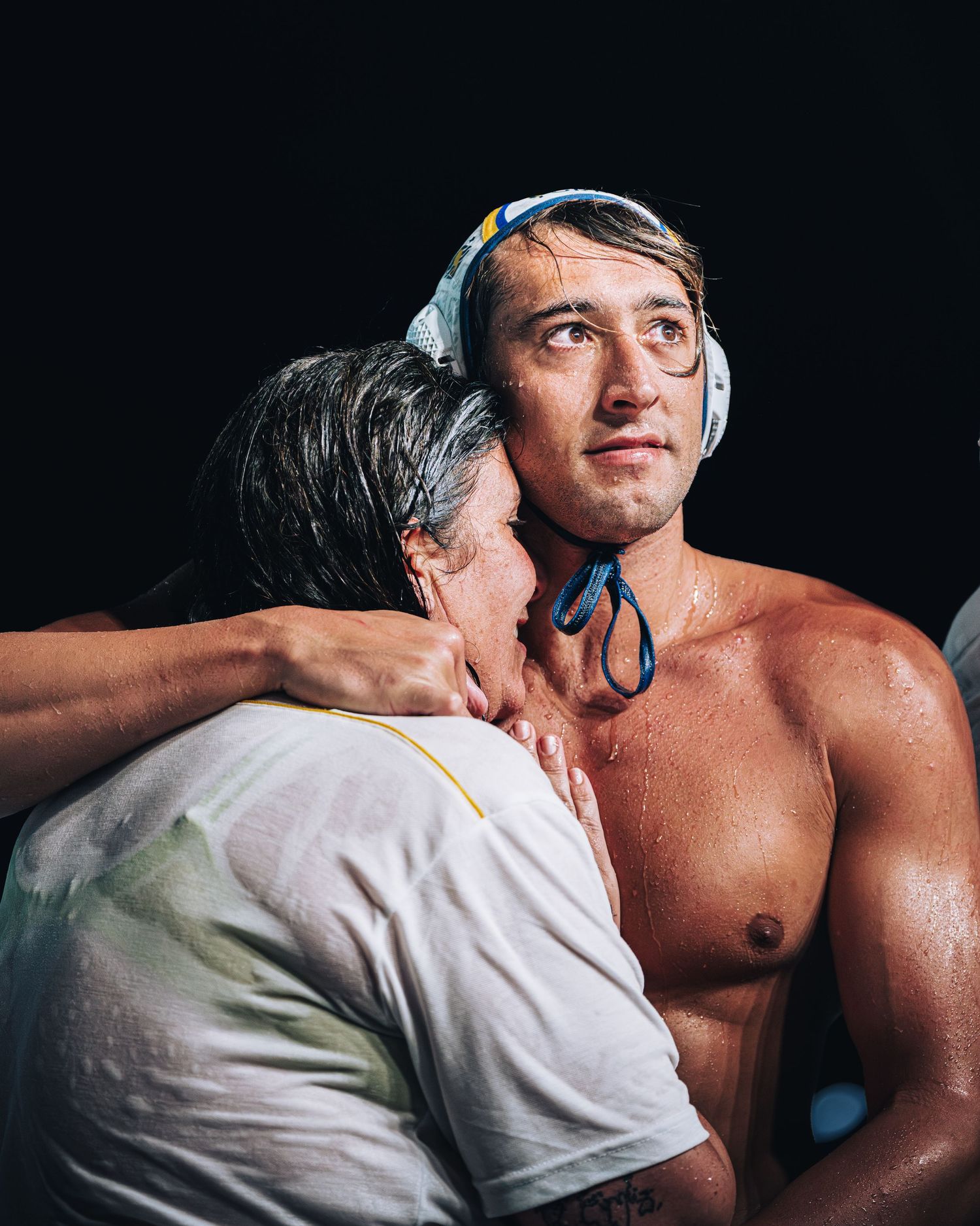 Water polo player in cap embracing coach after championship victory poolside.