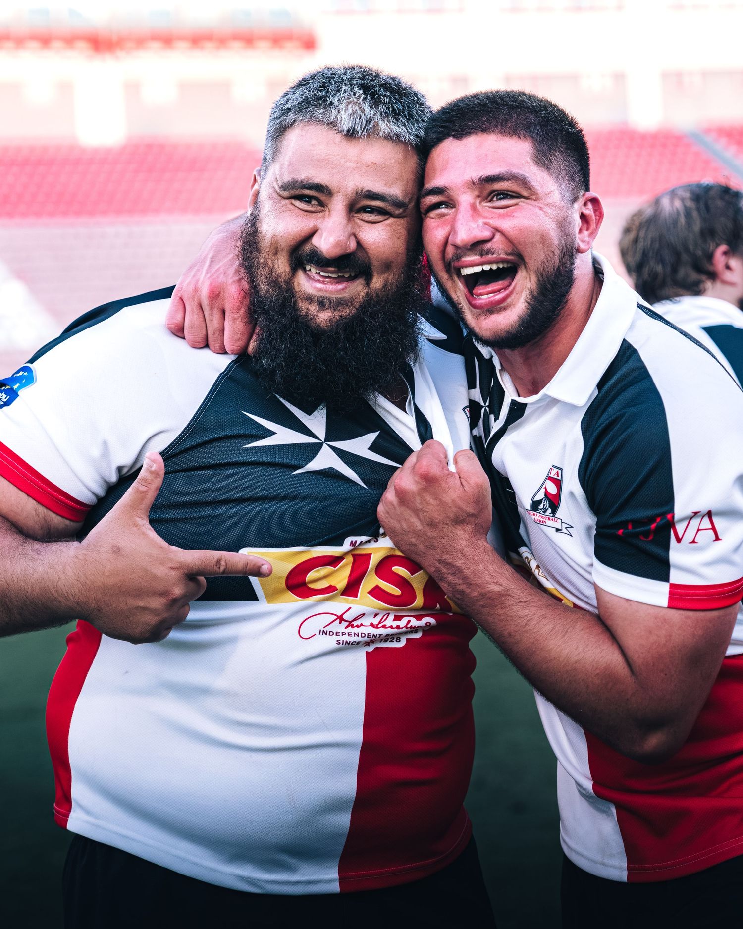 Two smiling rugby players in black and white jerseys celebrate together on the field.