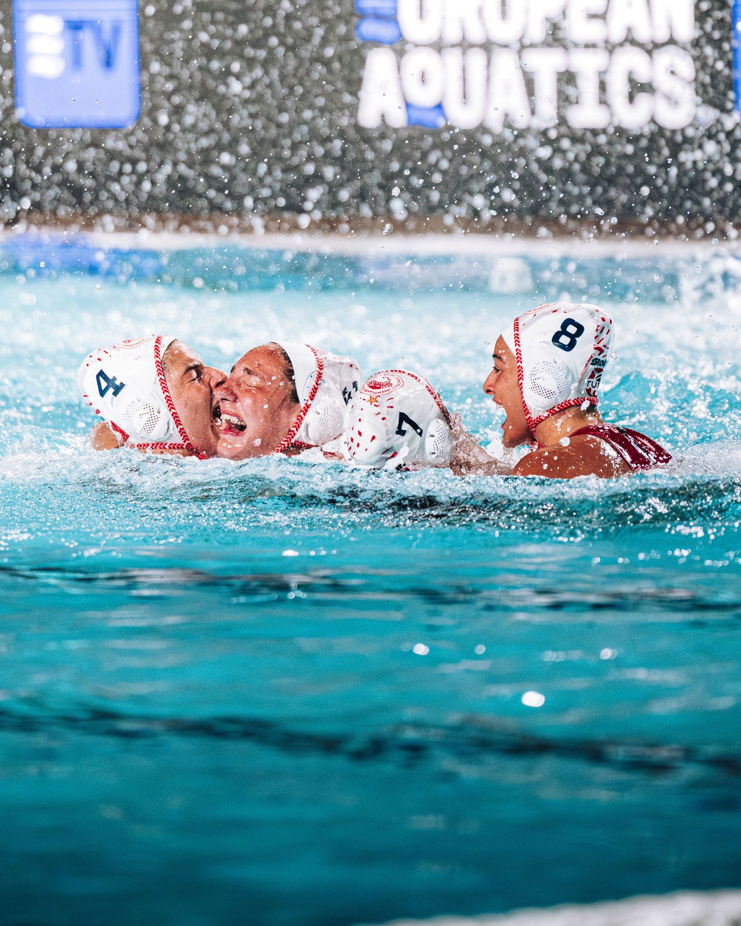 Two water polo players in white caps celebrating together in a pool at European Aquatics.