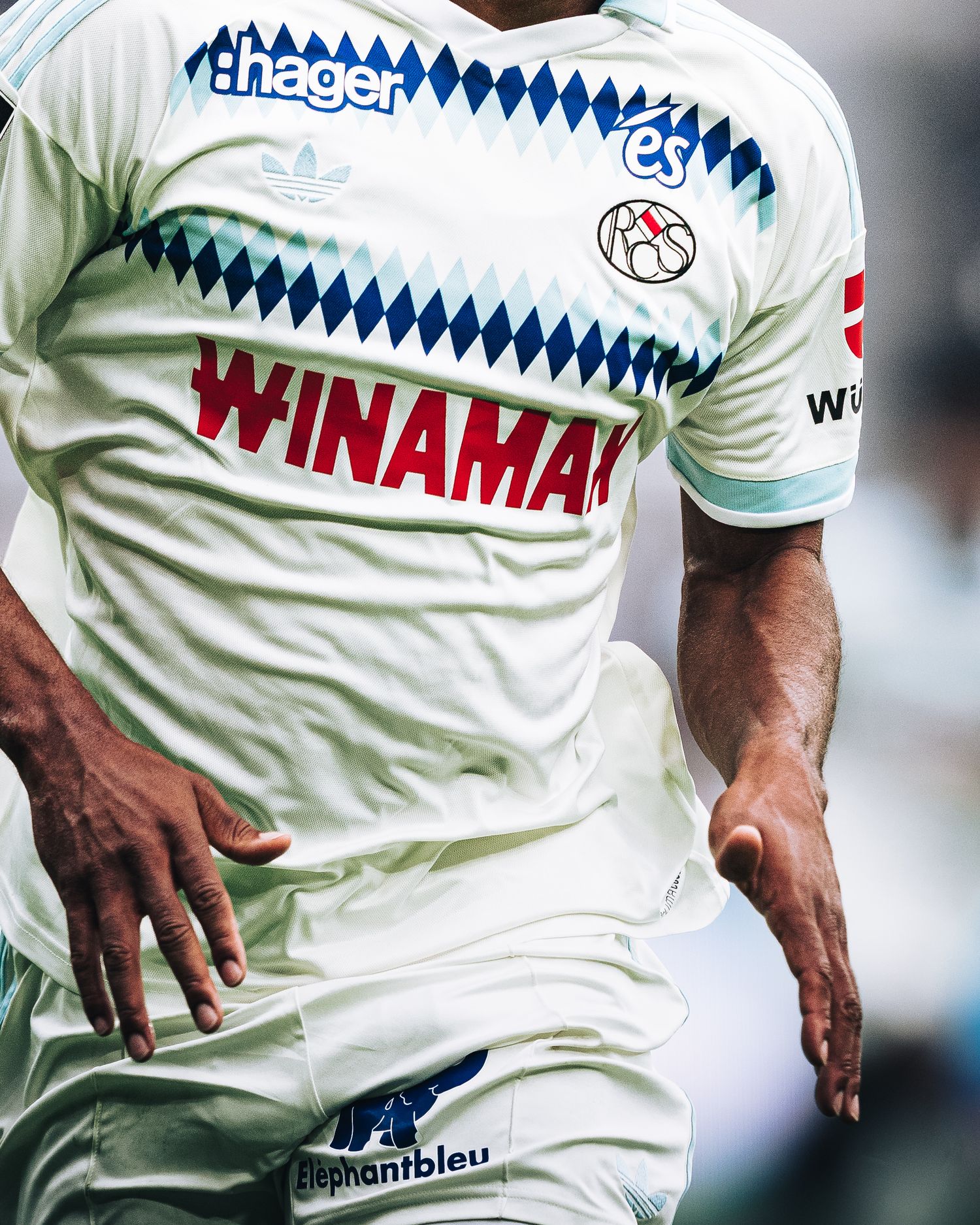 Footballer in white Adidas Winamax sponsored jersey runs during match close-up.