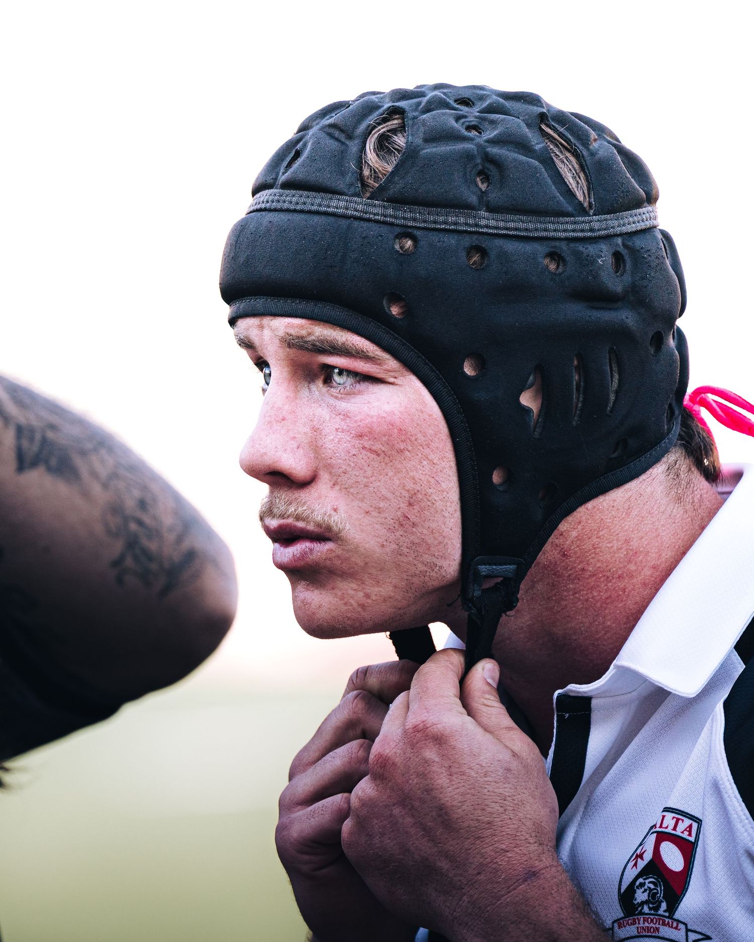 Young rugby player fastening leather scrum cap before competitive rugby match on field.