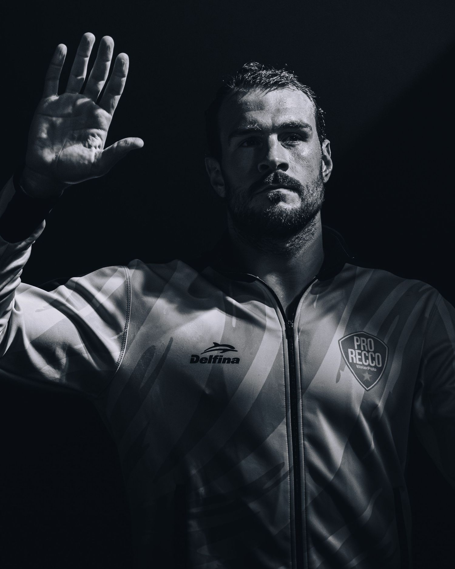 Black and white portrait of Pro Recco water polo player raising hand dramatically.