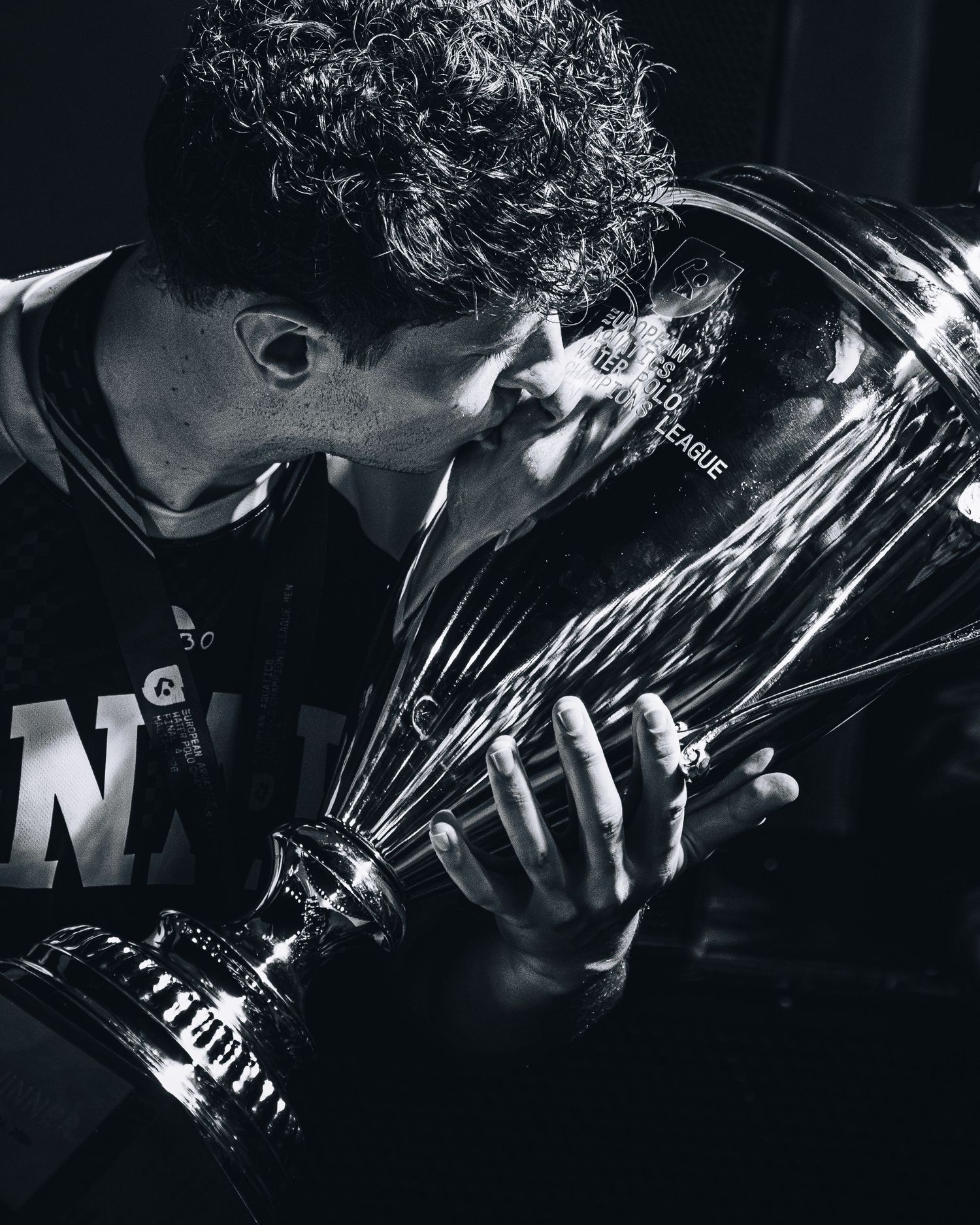 Black and white photo of athlete kissing Champions League water polo trophy.