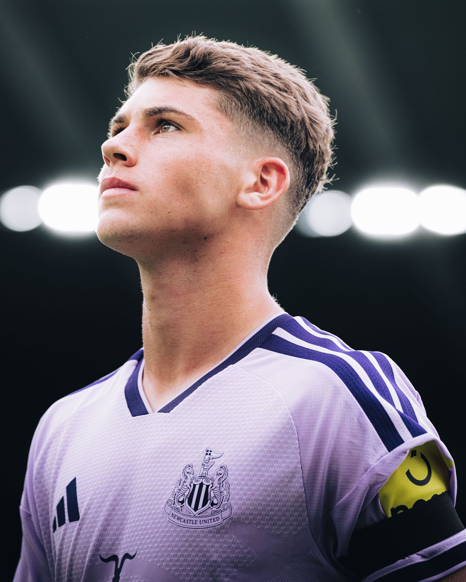 Young footballer in purple Newcastle United away kit looks upward on the pitch.