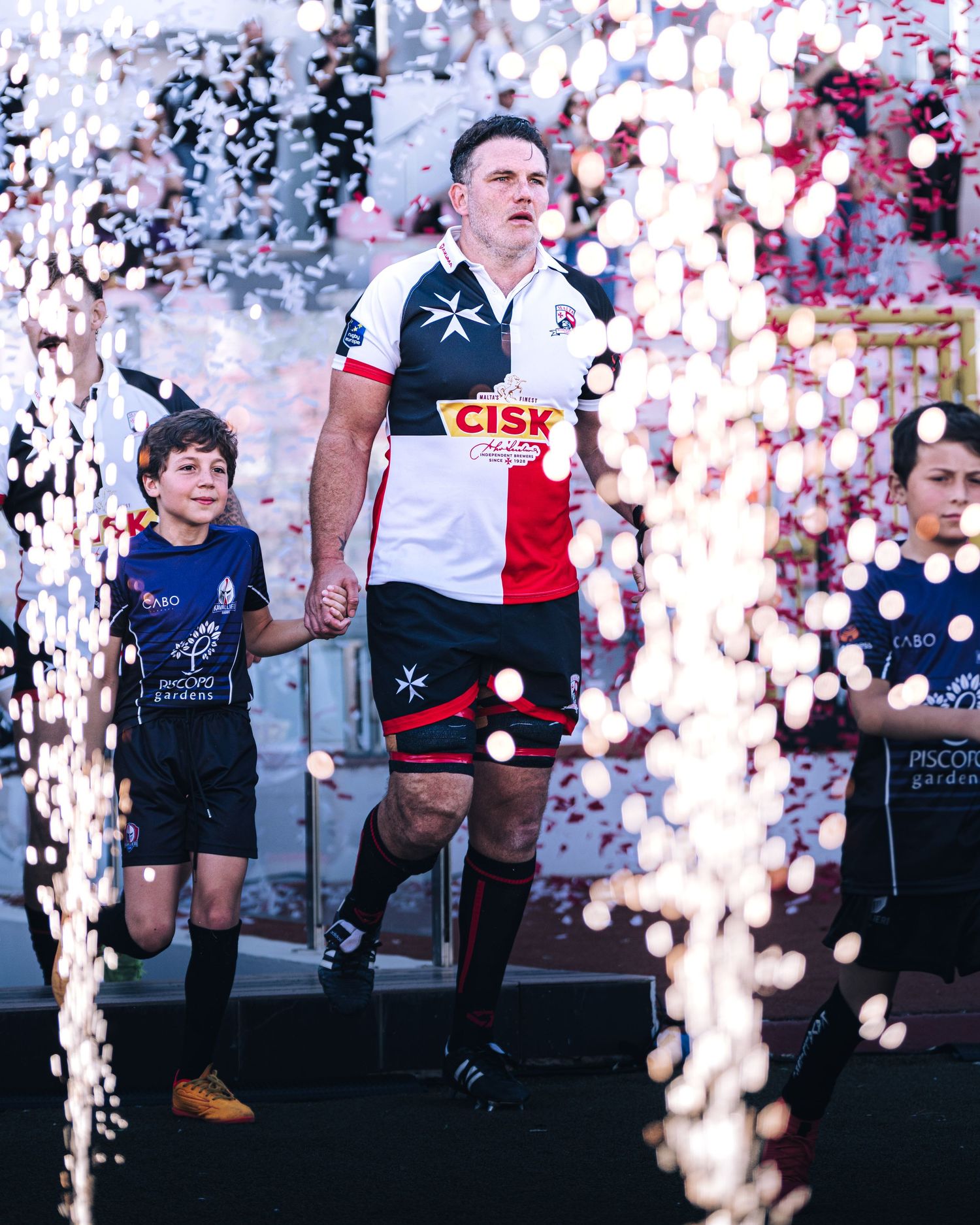Rugby player walking through confetti and pyrotechnics during dramatic stadium match entrance ceremony.