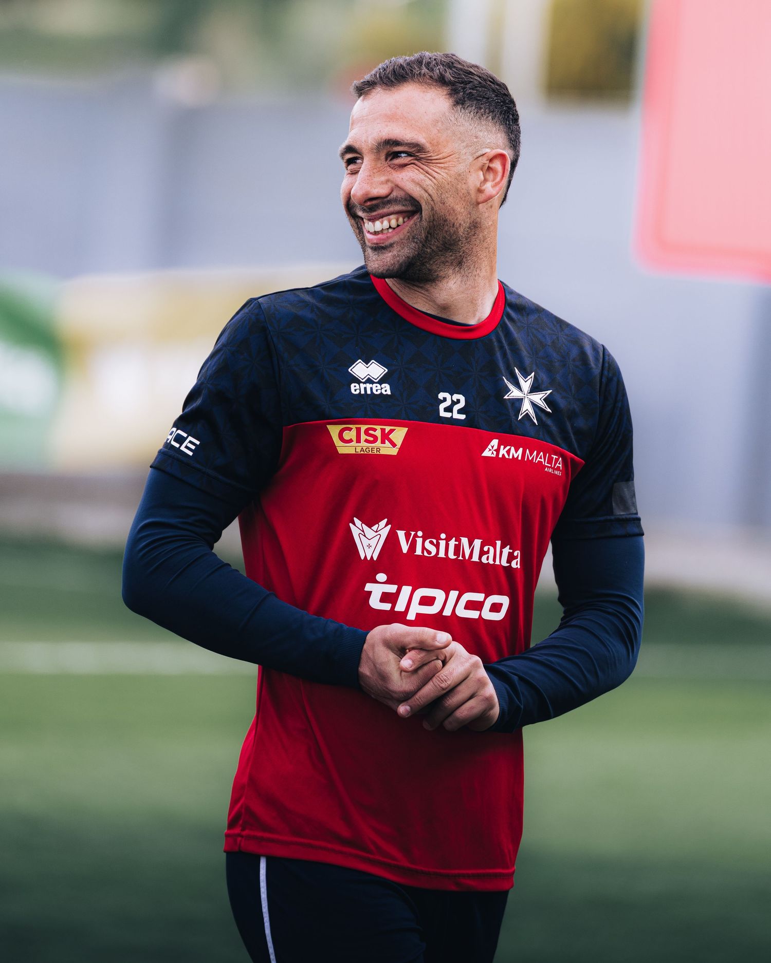 Smiling footballer in red and black Errea Malta national team jersey number 22 during training.