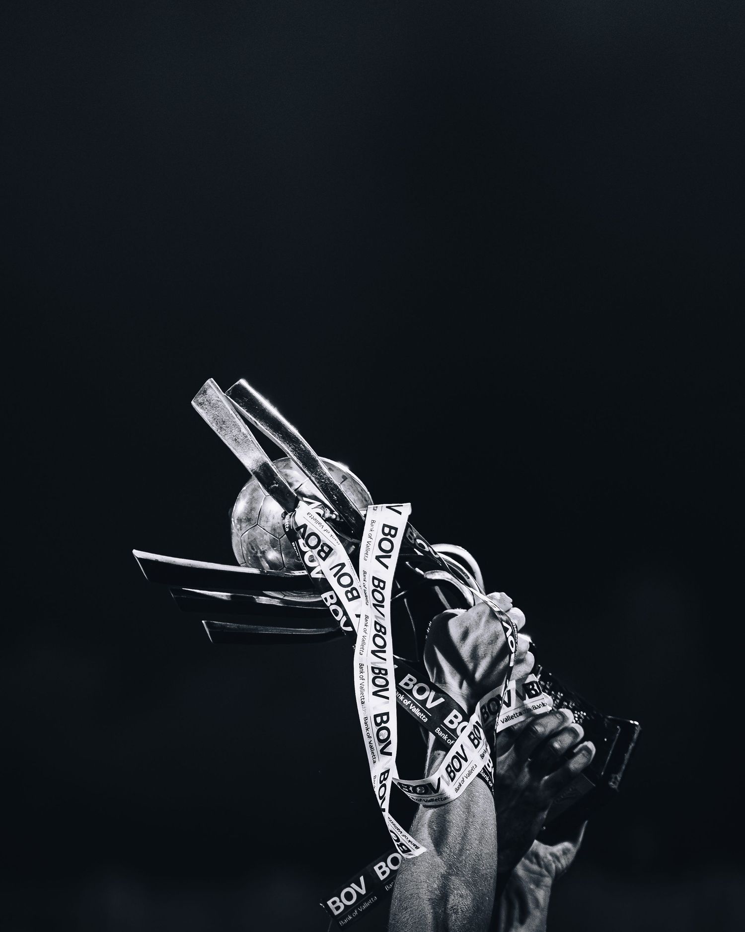 Black and white artistic photo of trophy being held up with decorative ribbon in darkness.