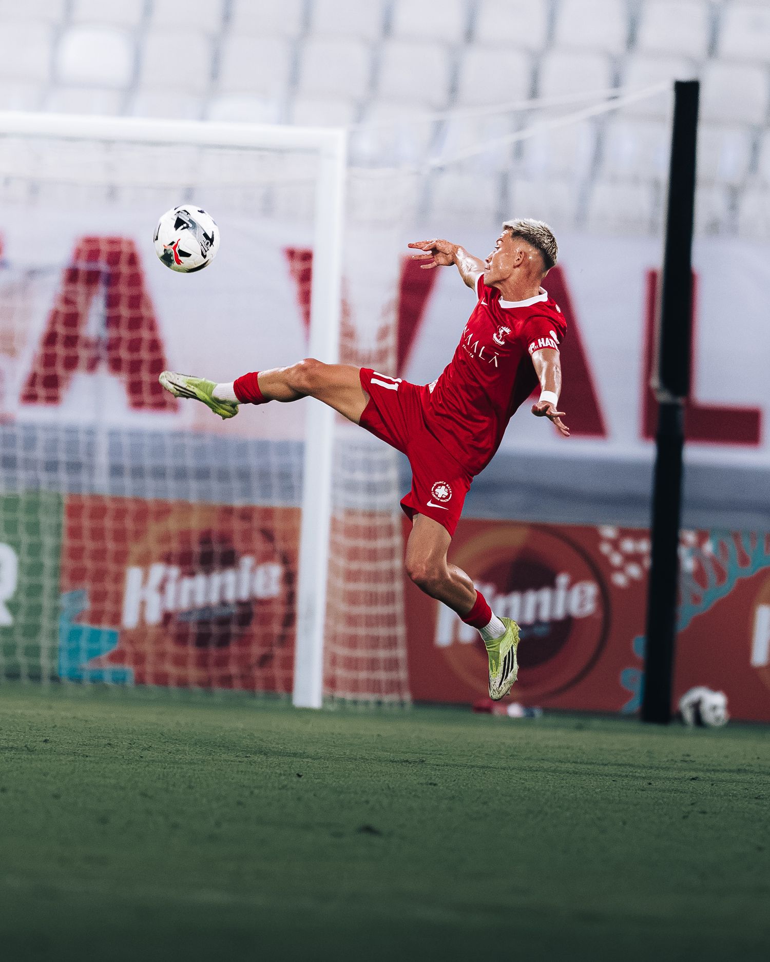 Dynamic soccer player in red kit performing acrobatic volley kick in front of goal.