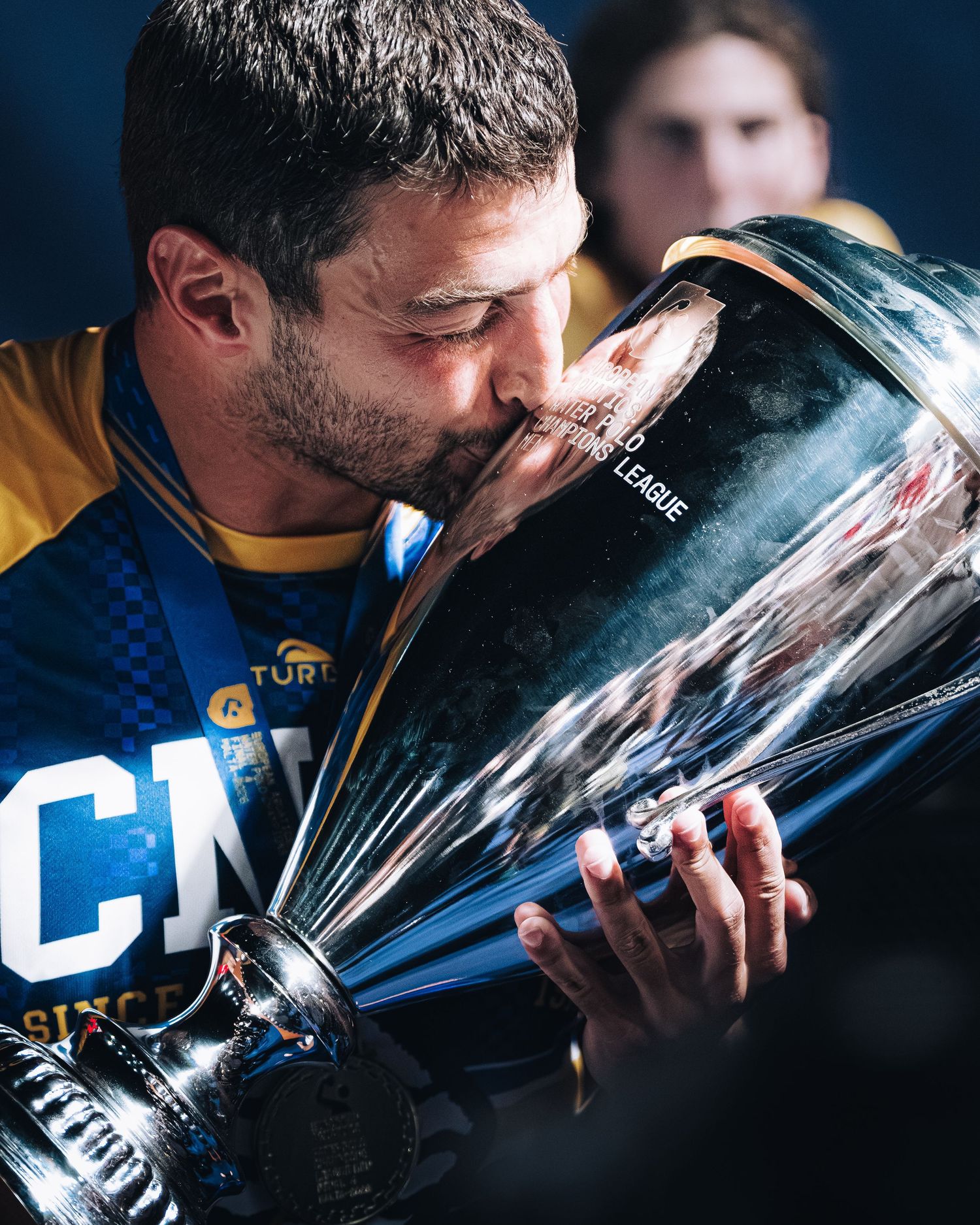Athlete kisses championship trophy in blue and yellow sports jersey celebrating victory.