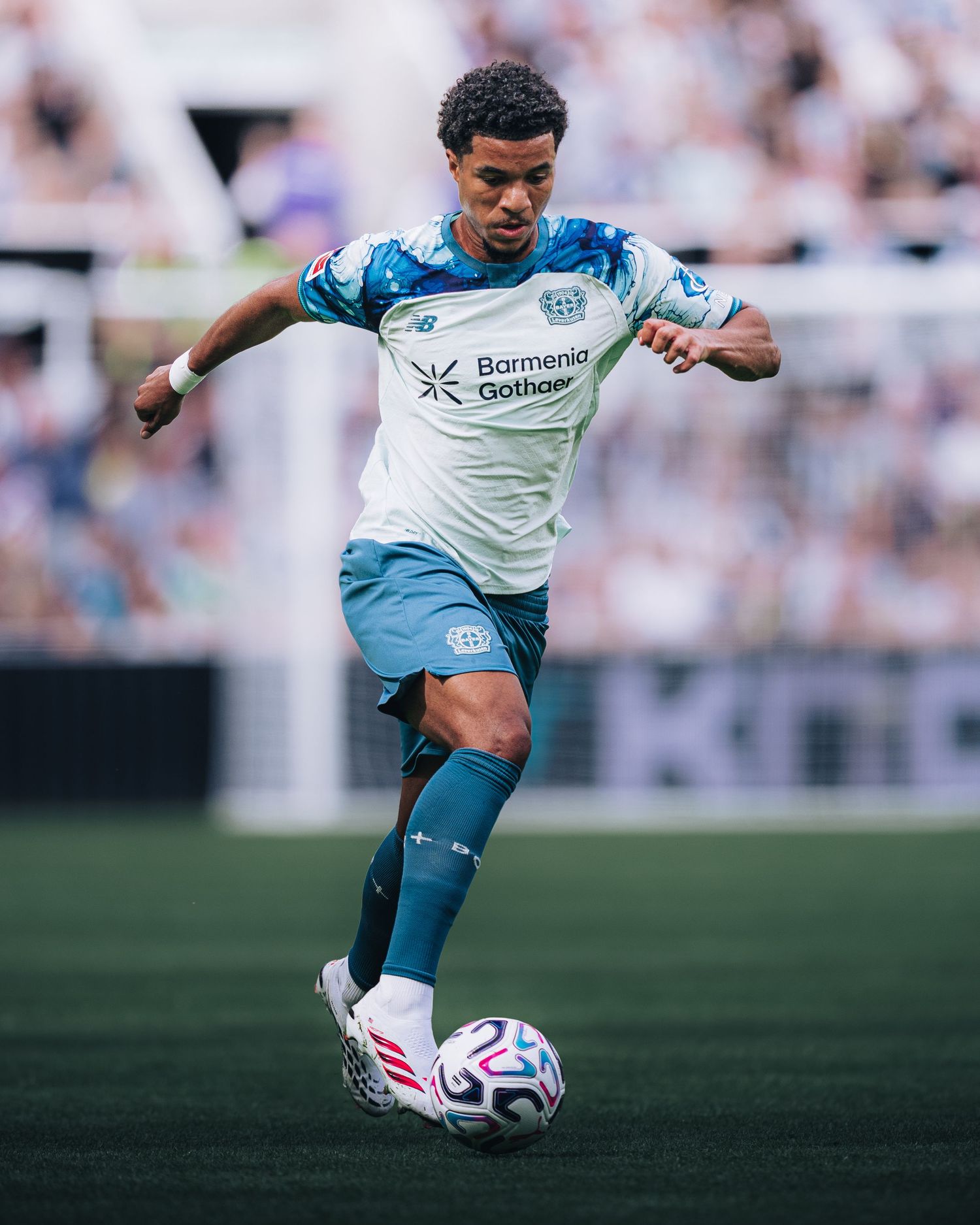 Soccer player in Bayer Leverkusen away kit dribbles ball during competitive match.