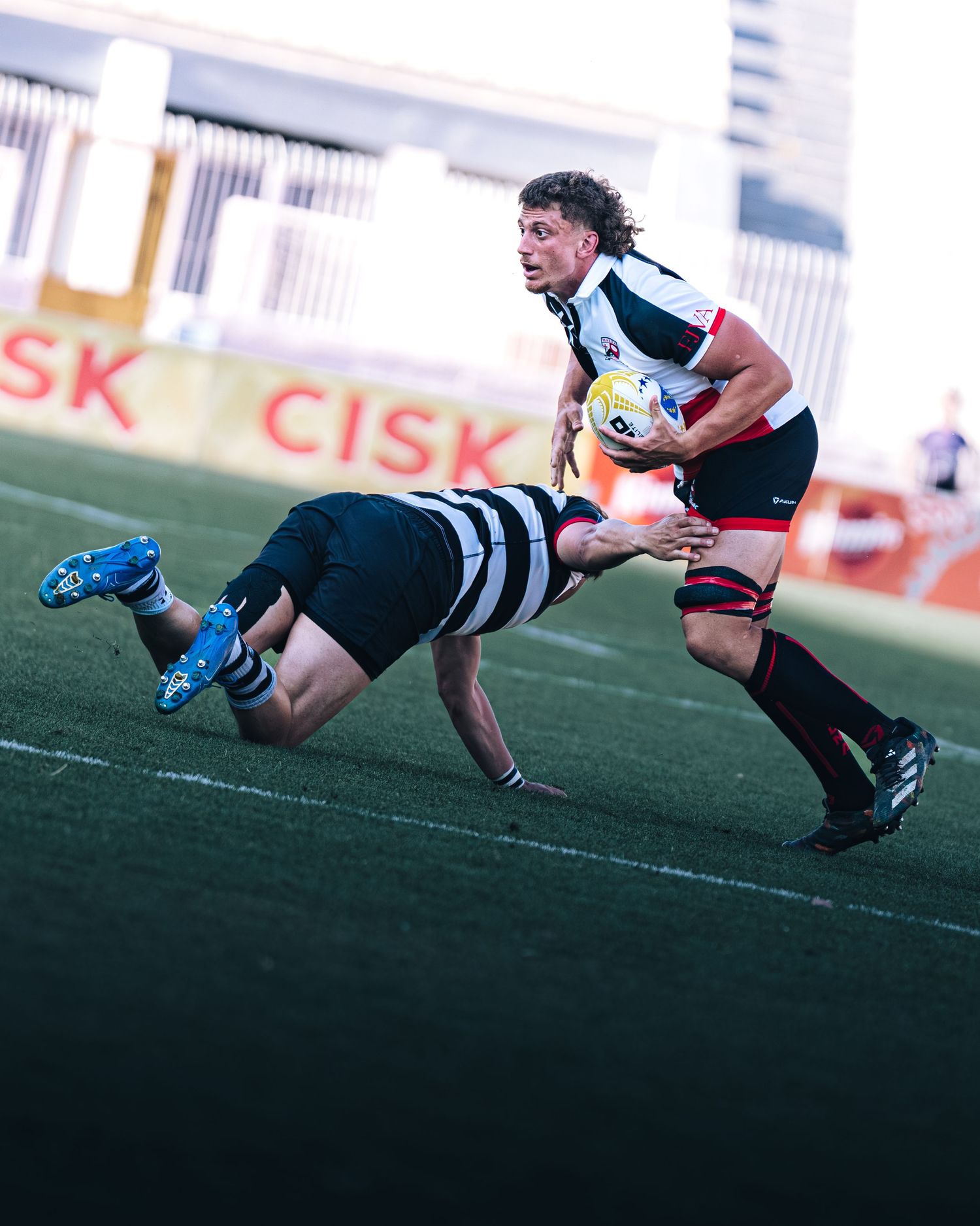 Malta rugby player evading tackle while carrying ball during competitive league match.
