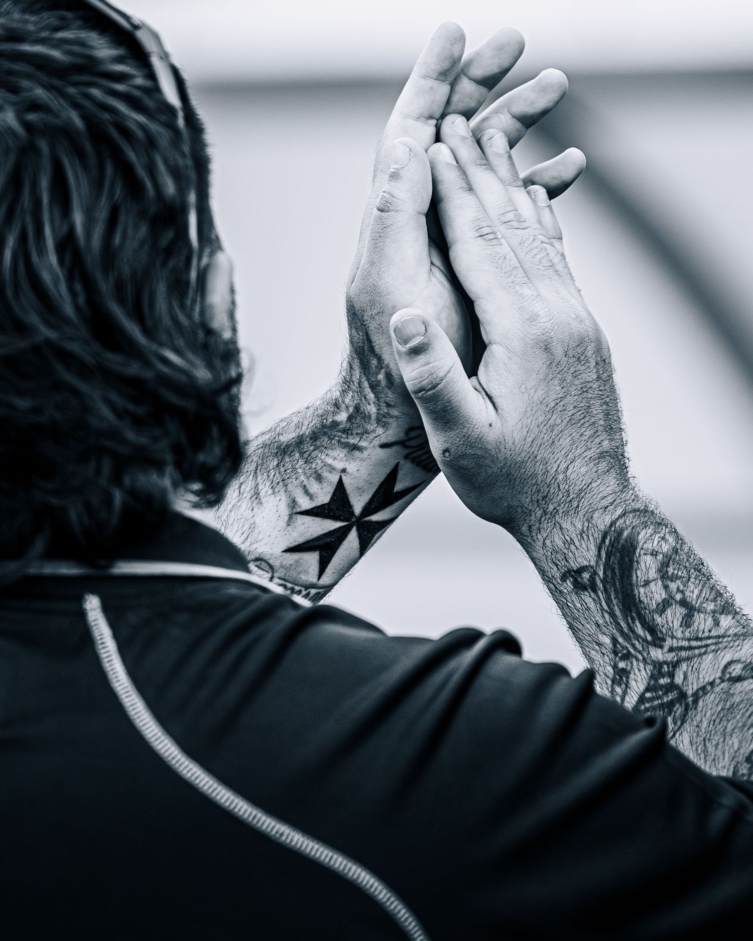 Black and white close-up of rugby player clapping hands showing Maltese cross neck tattoo.