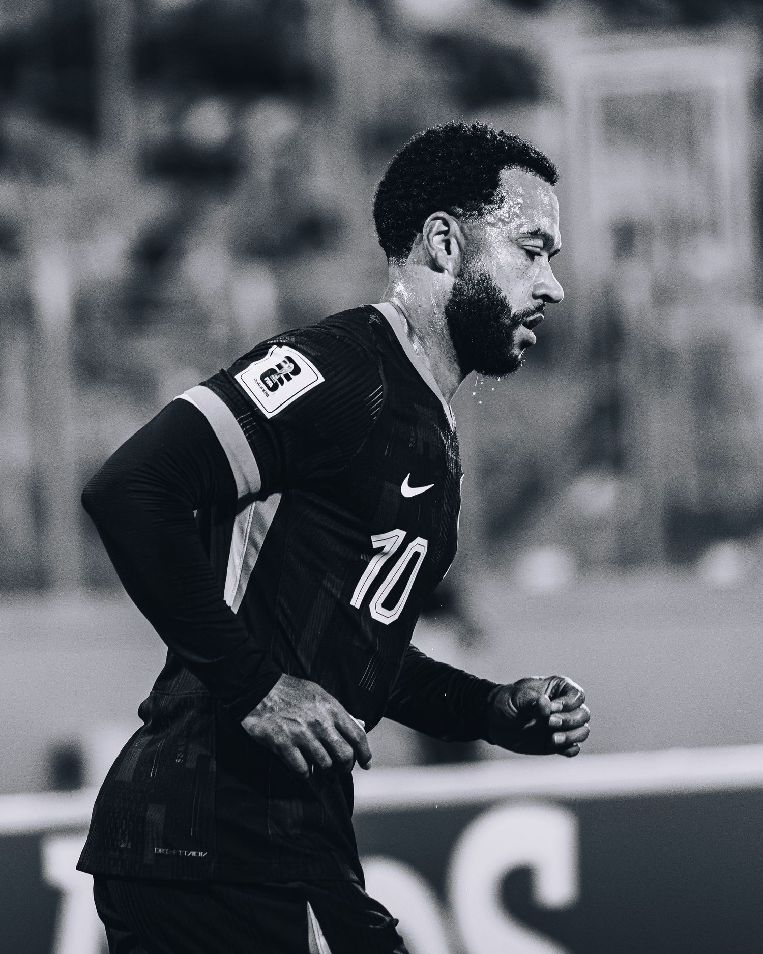 Black and white photo of a soaked footballer wearing number 10 Nike jersey running in the rain.
