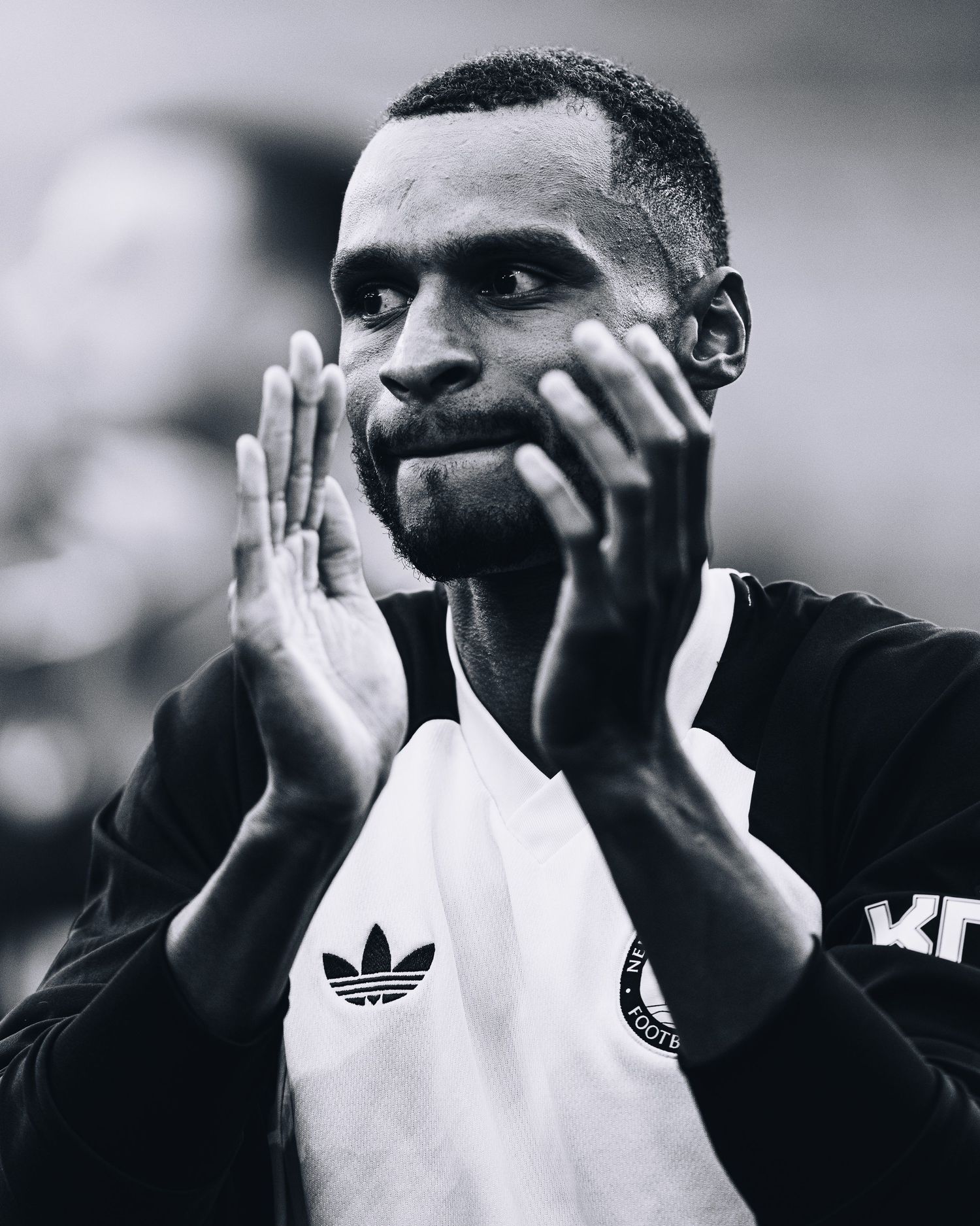 Black and white portrait of soccer player in Adidas jersey clapping hands together appreciatively.