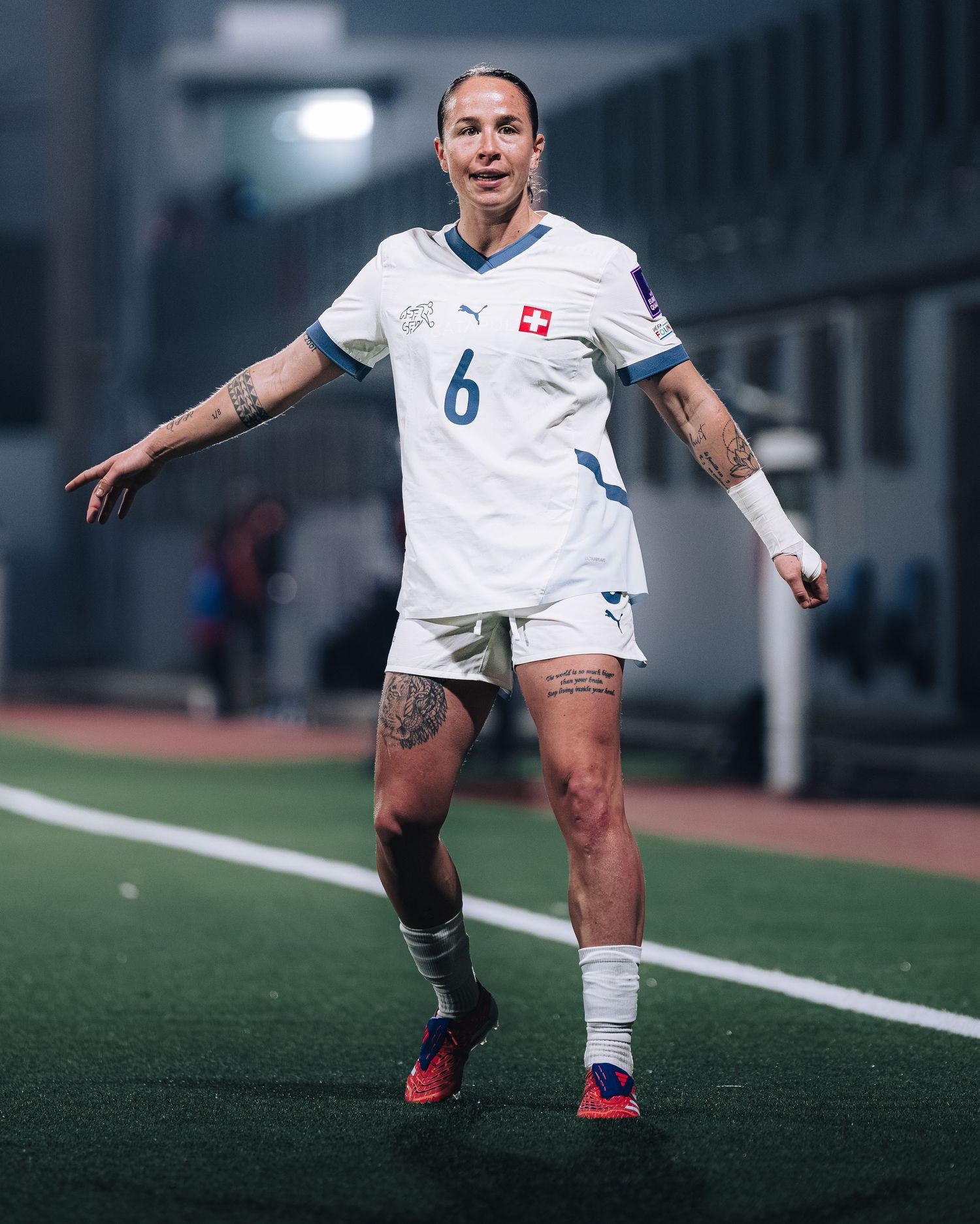 Female Swiss footballer in white Puma kit number 6 with tattoos gesturing during a match.