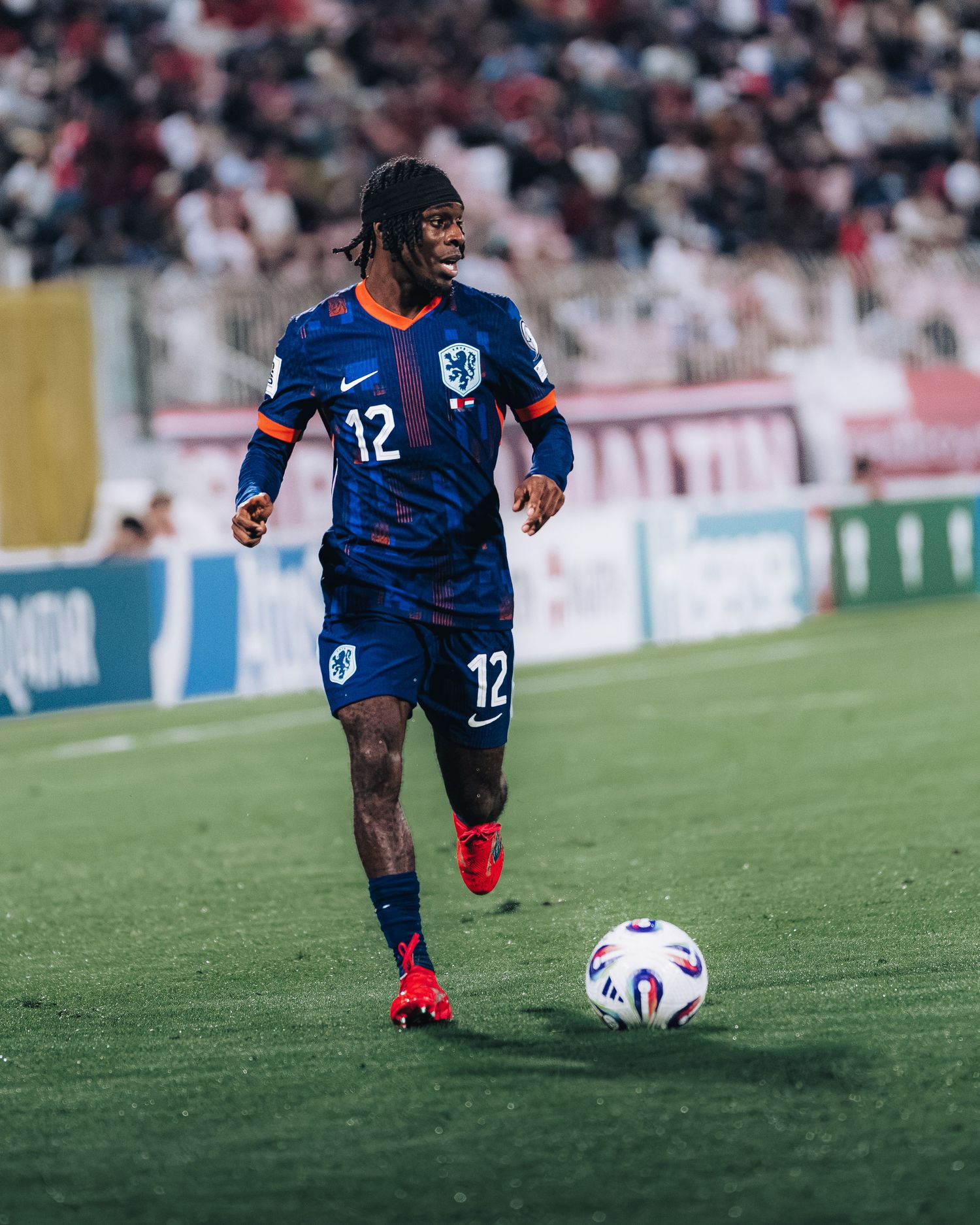 Soccer player wearing blue Nike jersey number 12 dribbles ball on green field during match.