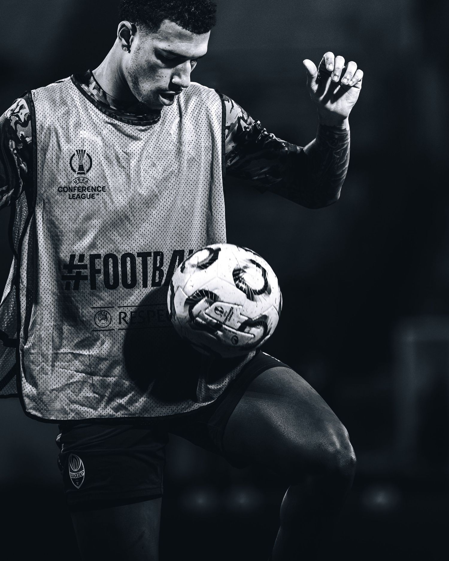Black and white photo of footballer in Conference League bib balancing ball on knee.