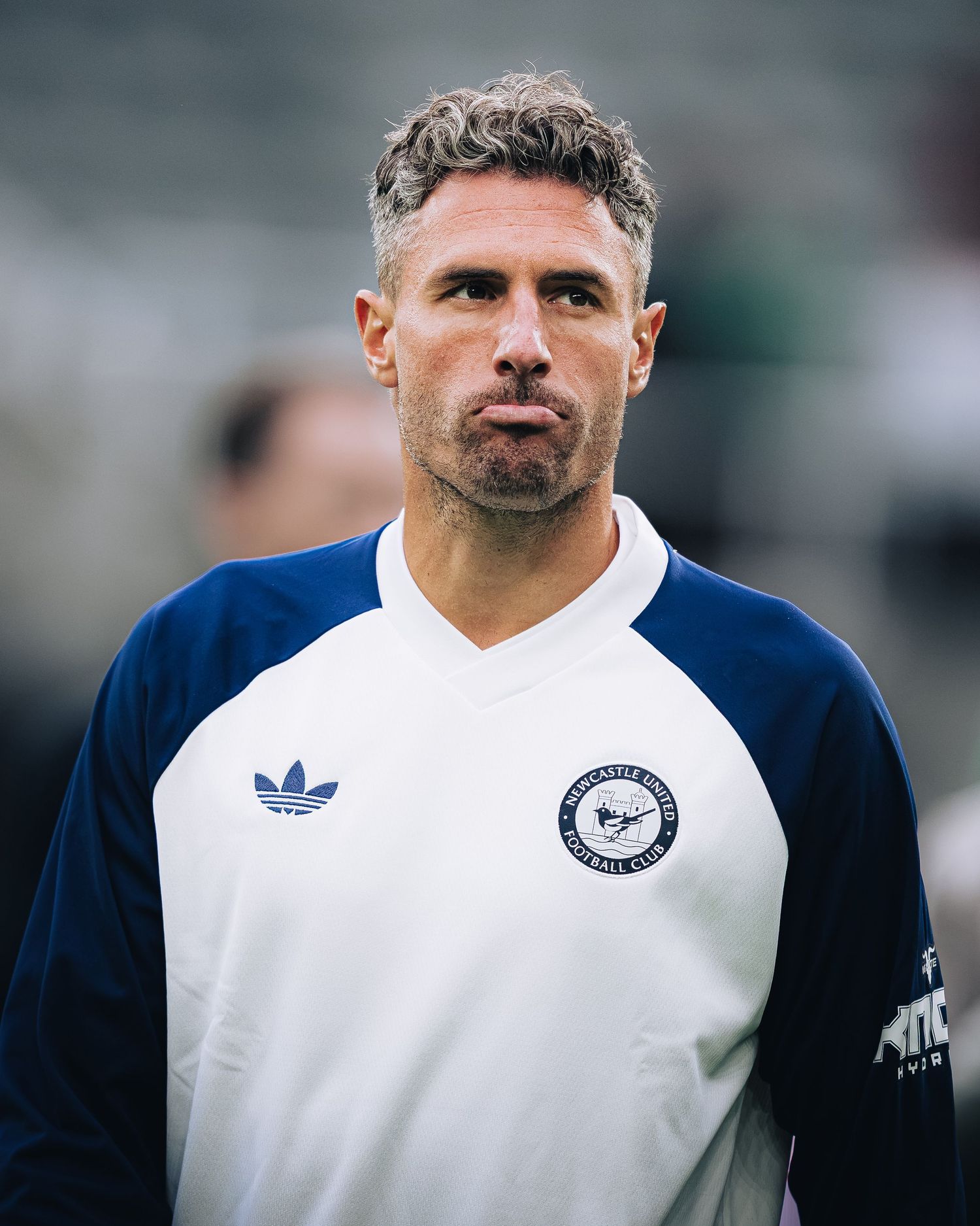 Male soccer coach in white and navy Adidas Newcastle FC training top looks focused on sideline.