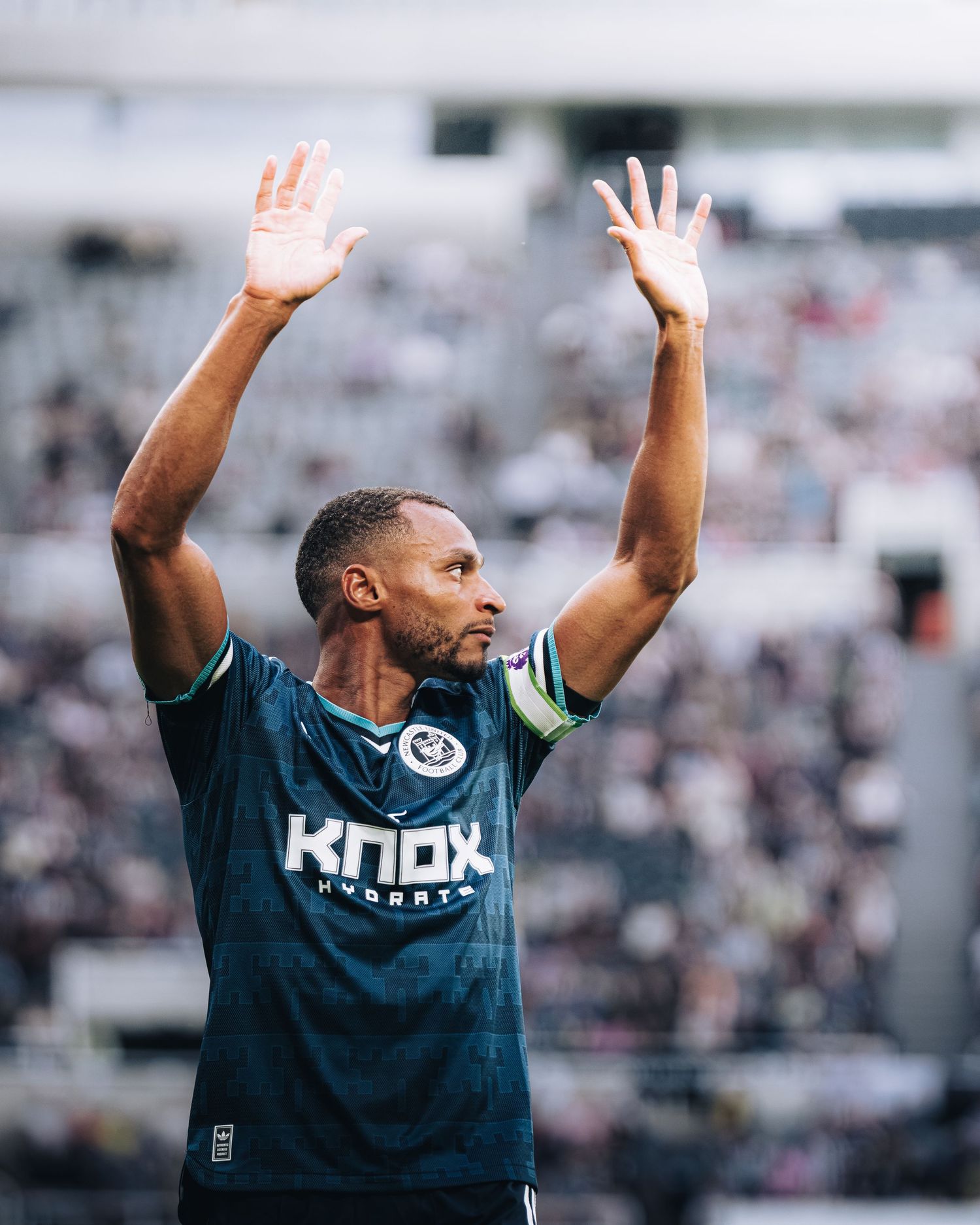 Soccer player in Knox Hydrate dark jersey raises both hands to crowd in packed stadium.