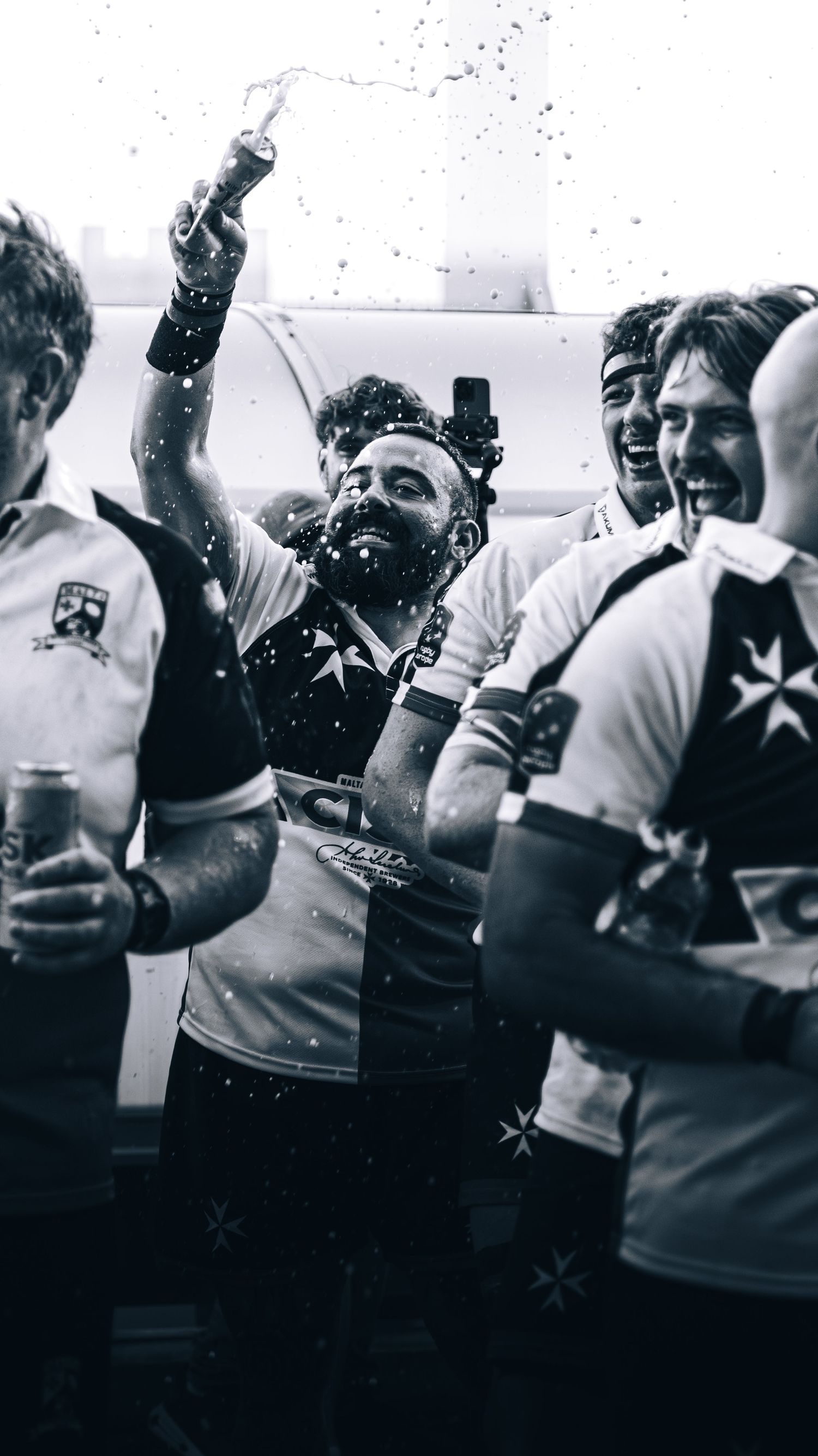 Black and white photo of rugby players celebrating with champagne in a locker room.