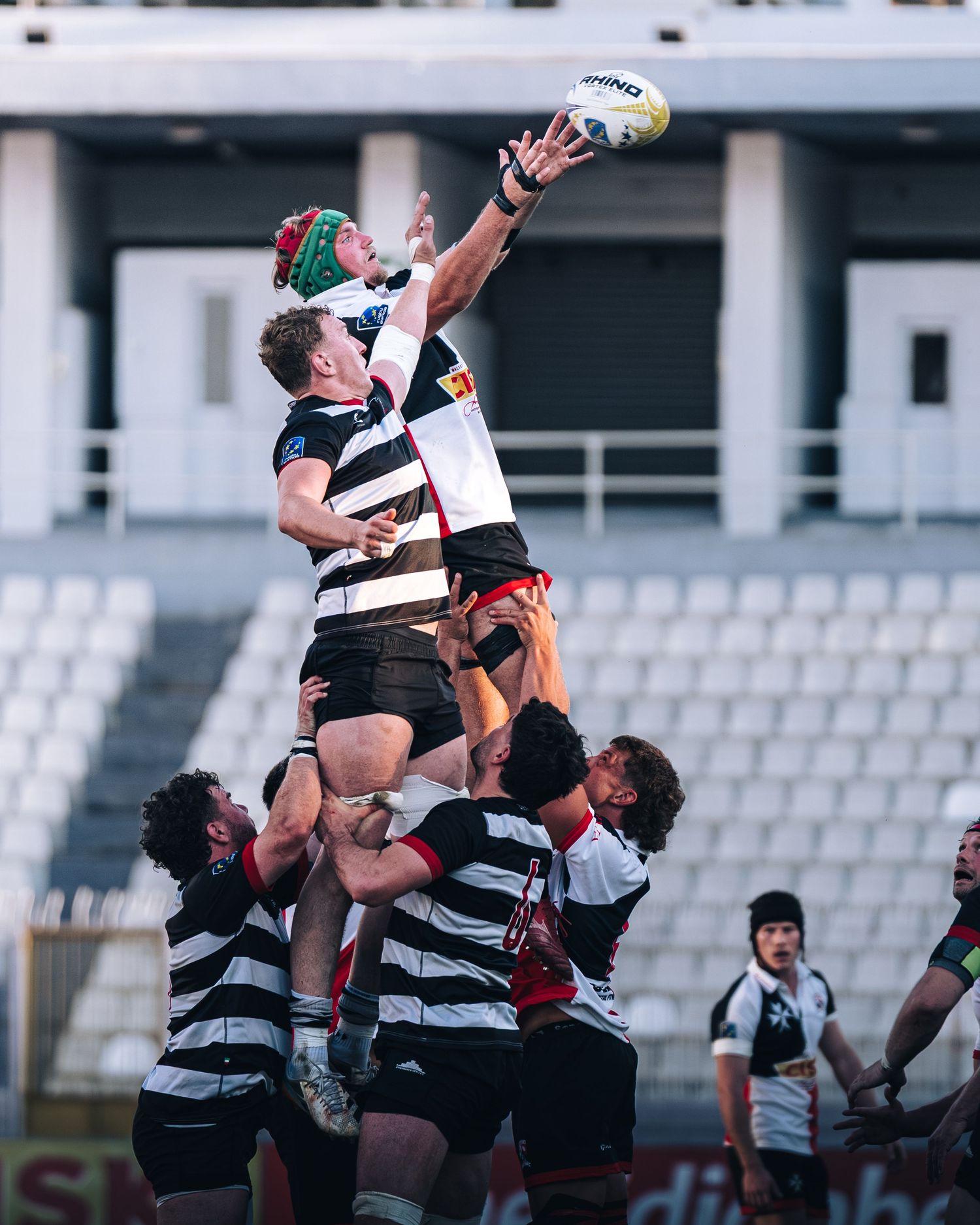 Rugby players compete in a lineout, with one player lifted high to catch the ball.