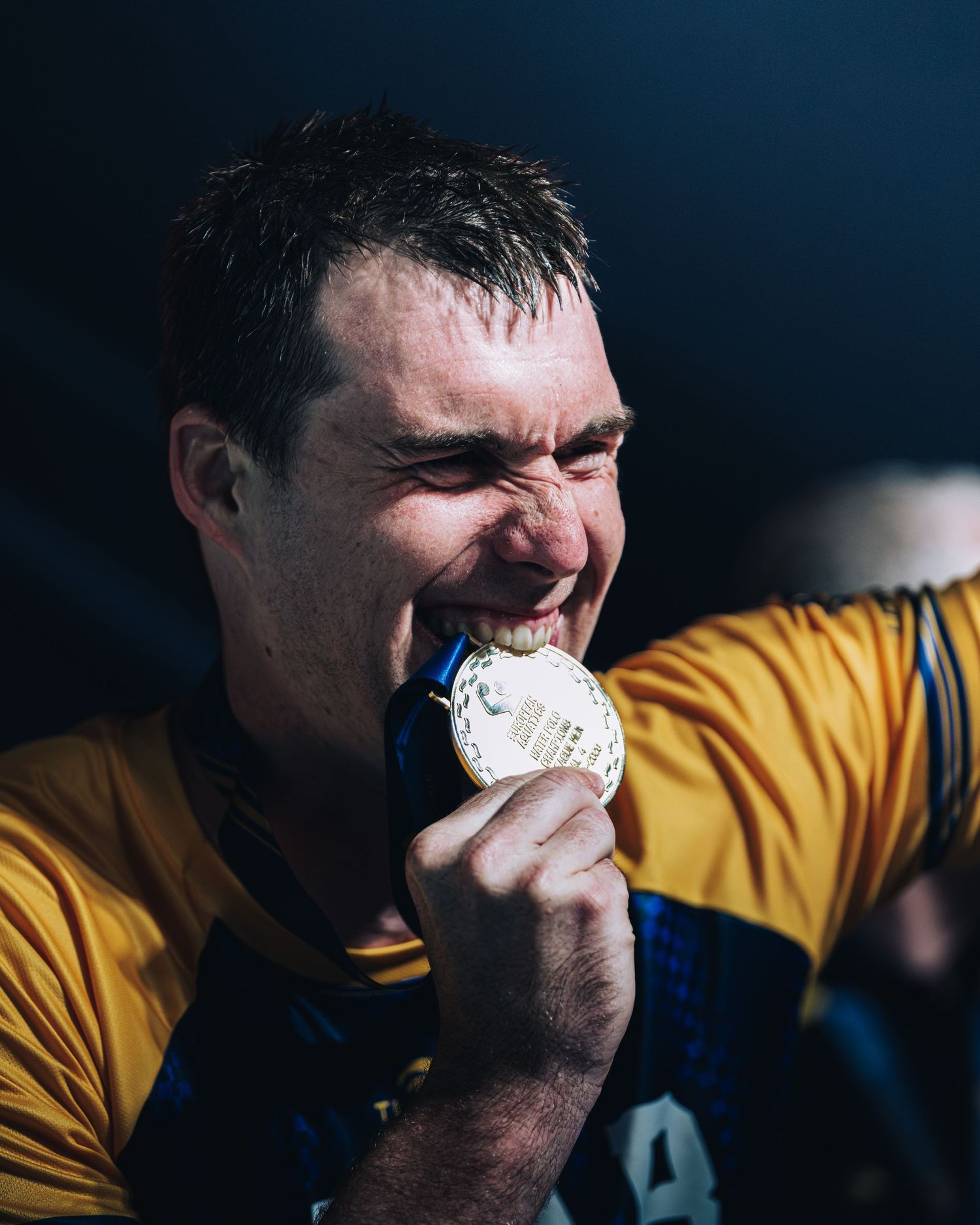 Jubilant male athlete biting gold medal celebrating victory in water polo championship.